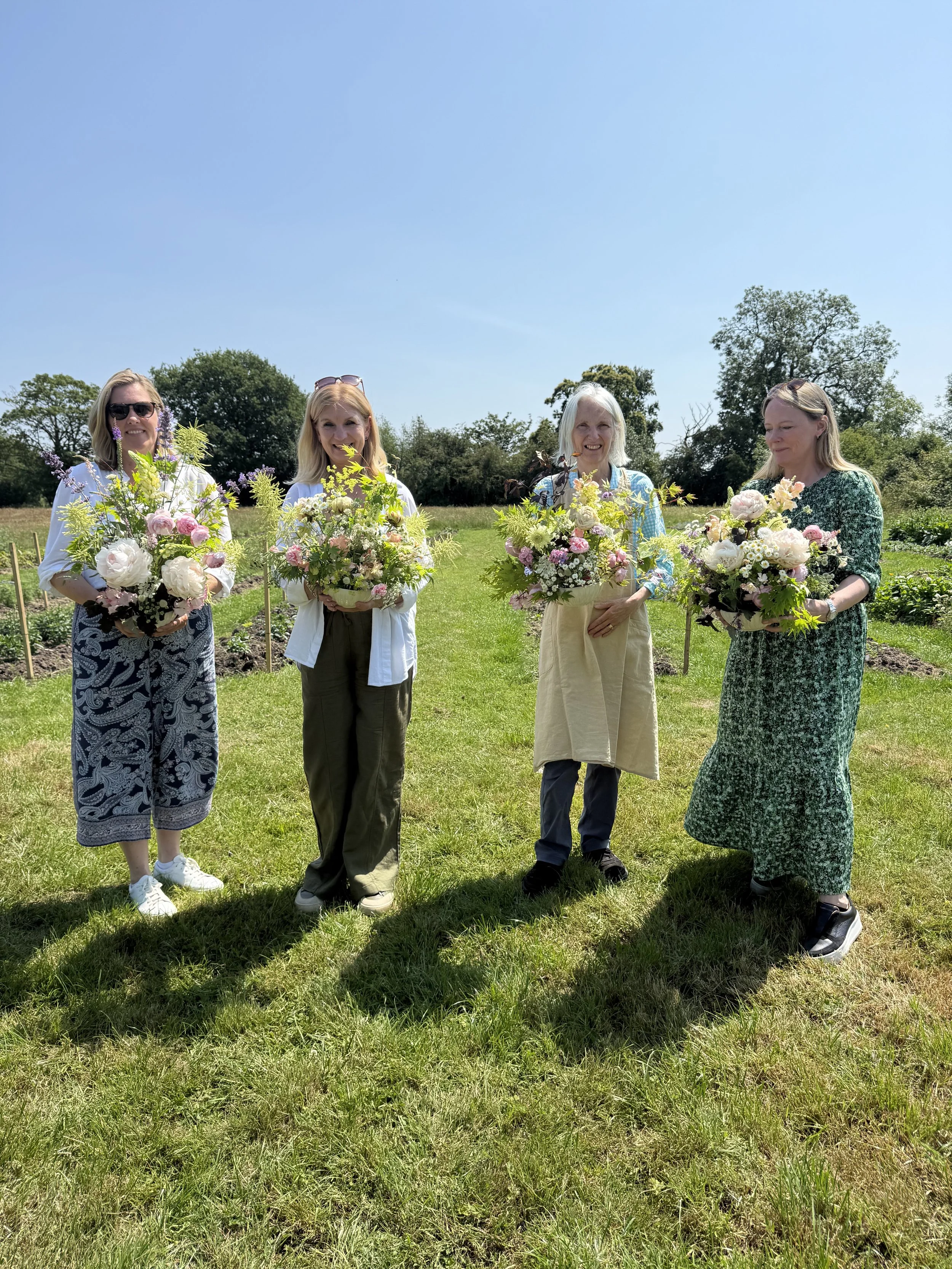 Ladies holding floral arrangements they created during a flower farm workshop, standing outdoors on a flower farm.