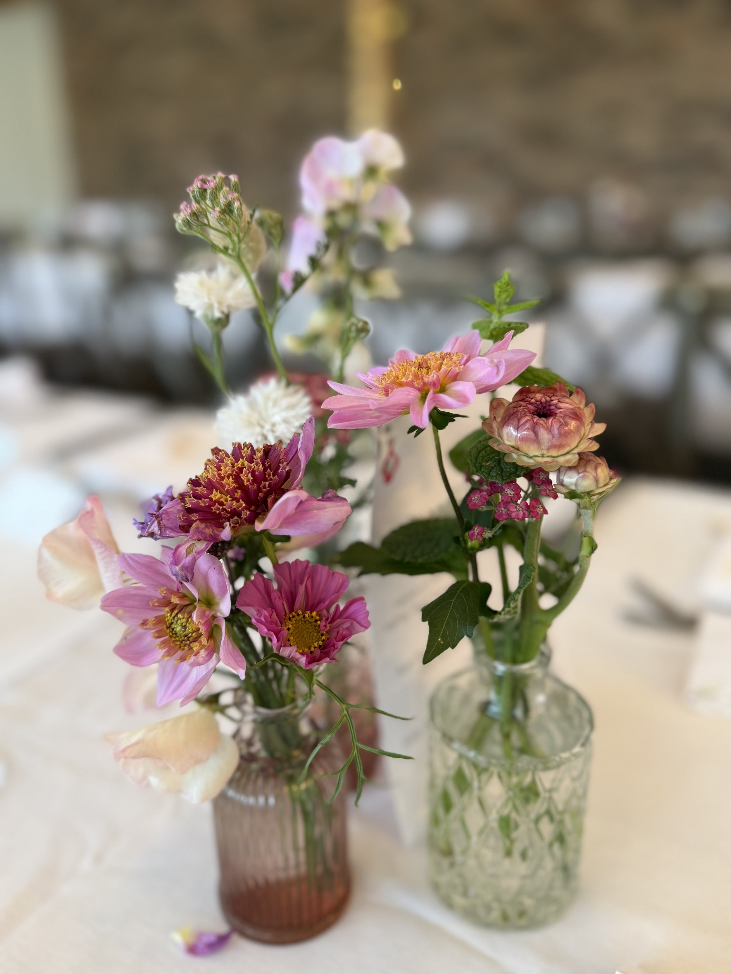 Two small vases with pink and white flowers on a table.