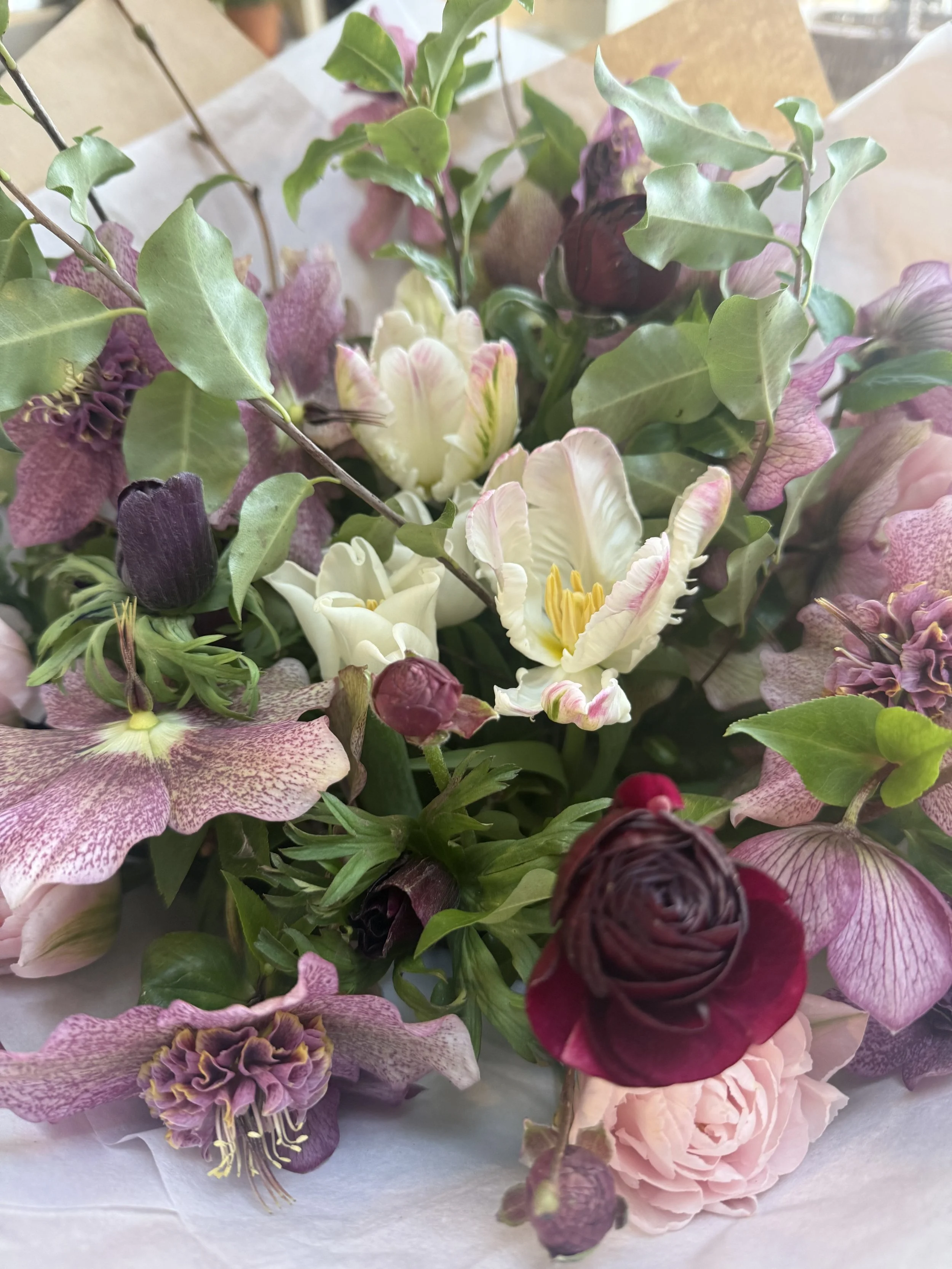 A bouquet of mixed flowers including pink, white, purple, and cream-colored blooms with green leaves.