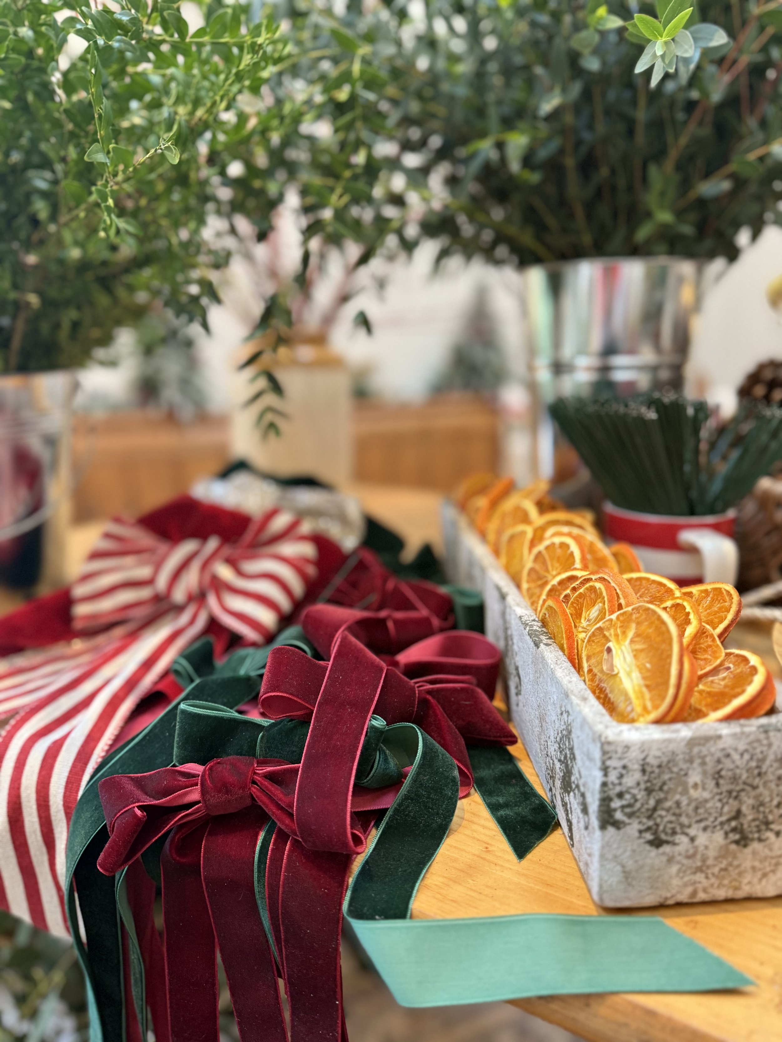 Decorative table with red and green velvet ribbons, a striped cloth, dried orange slices, and greenery in a festive setting.