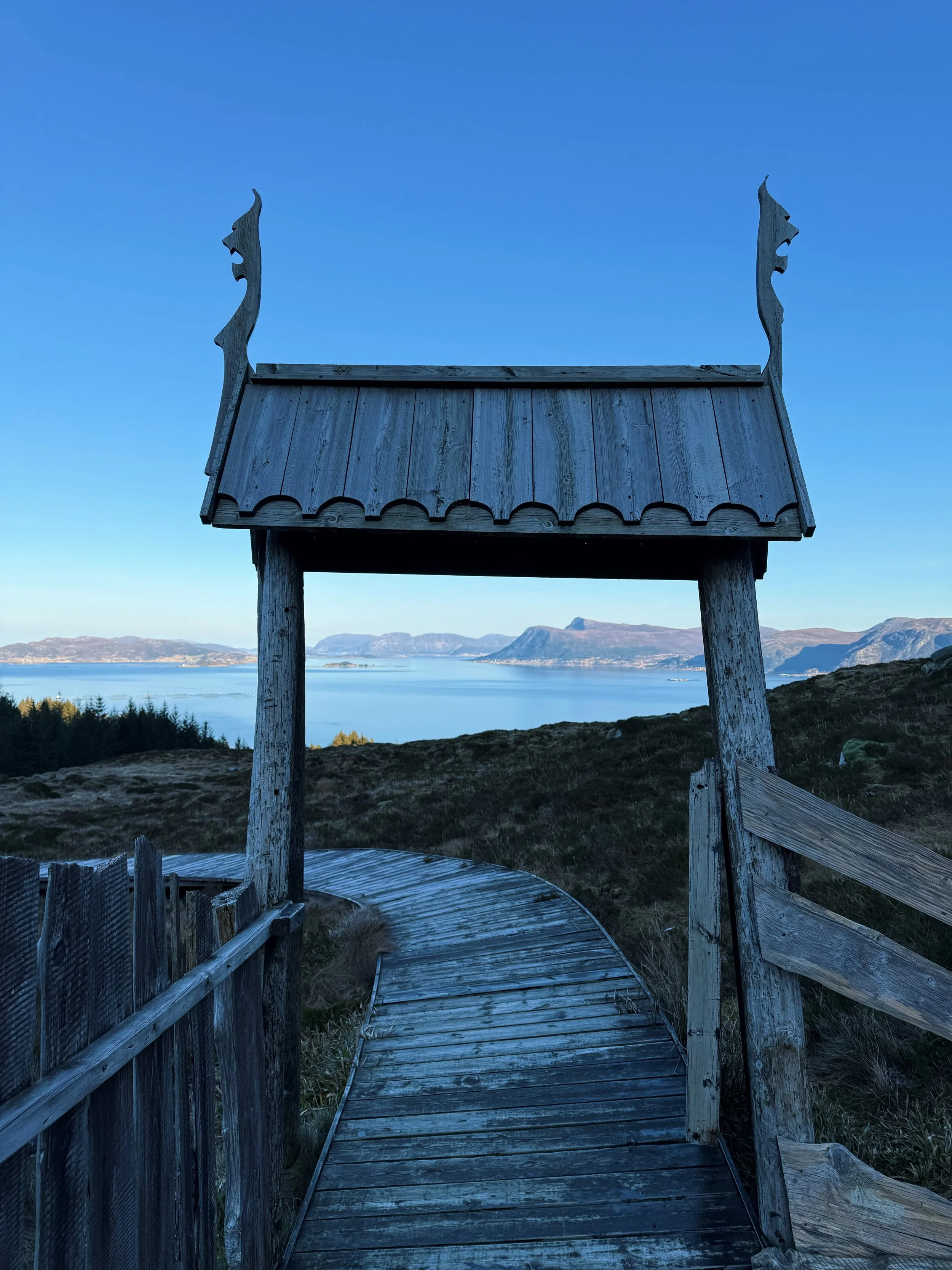 Wooden path and gate with dragon carvings leading to scenic ocean view.