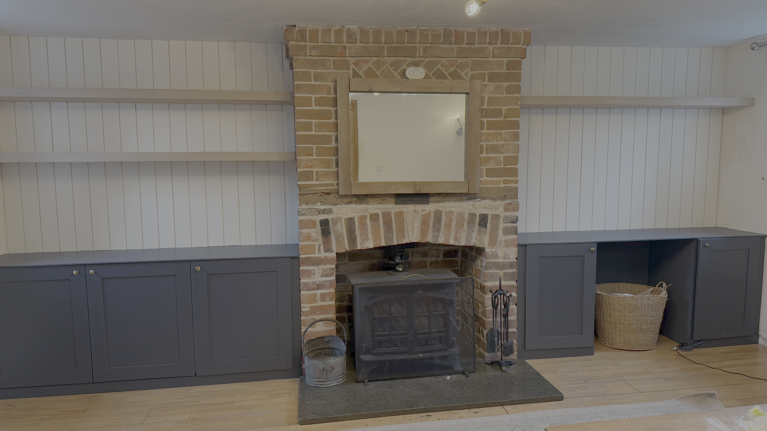 Living room with brick fireplace, mirror above, dark blue cabinets on both sides, and wooden floors.