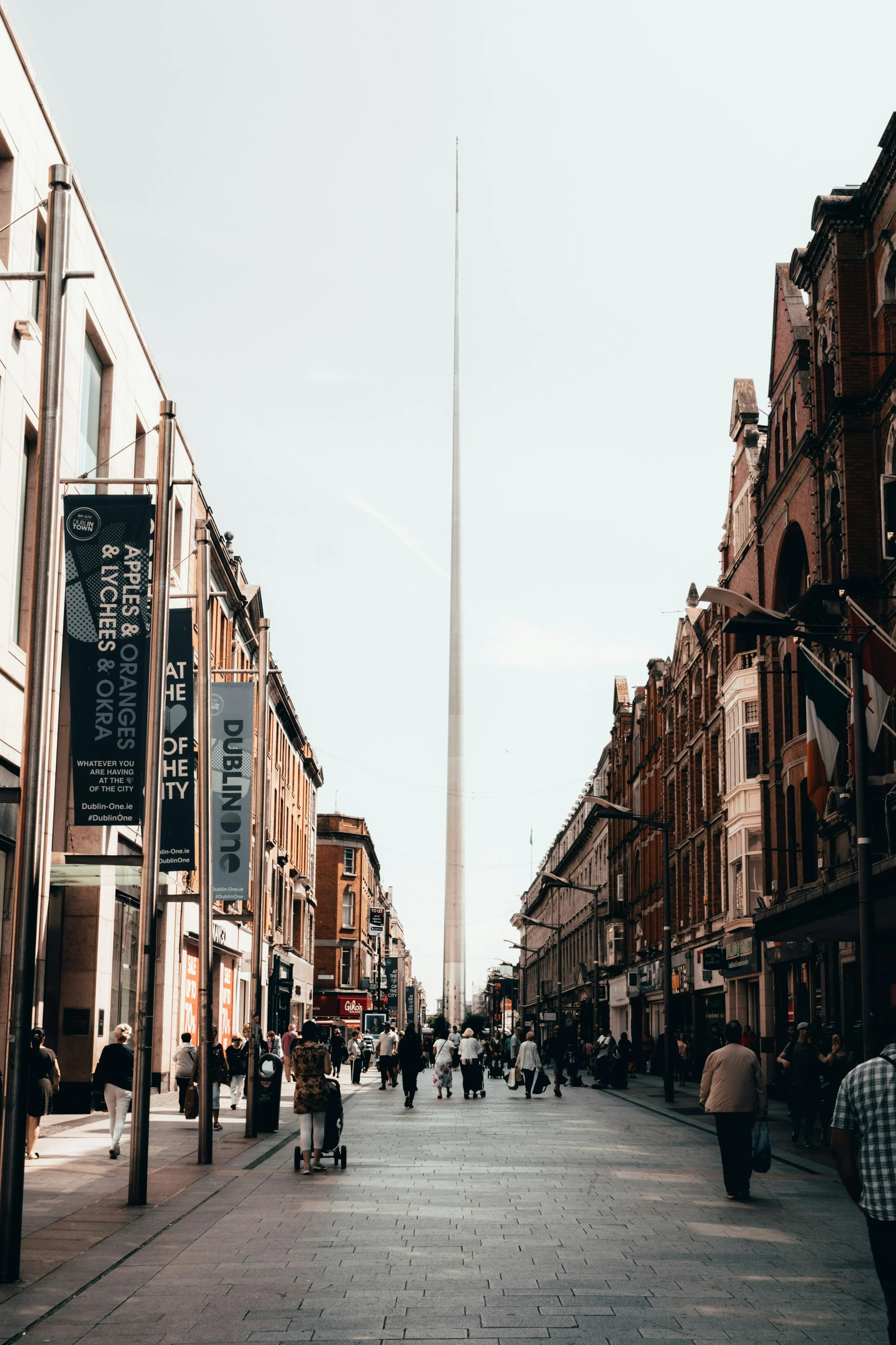Street view of Dublin's Spire on O'Connell Street, with pedestrians and shops.