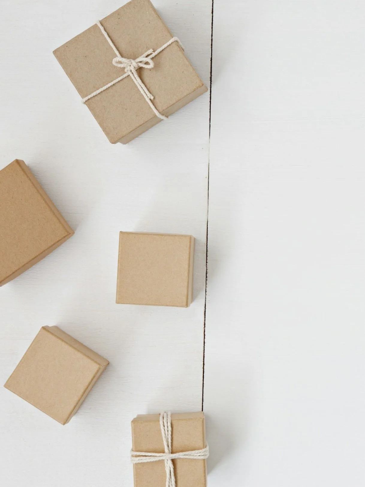 Several small gift boxes wrapped in plain brown paper, some tied with white string, are arranged on a white surface.