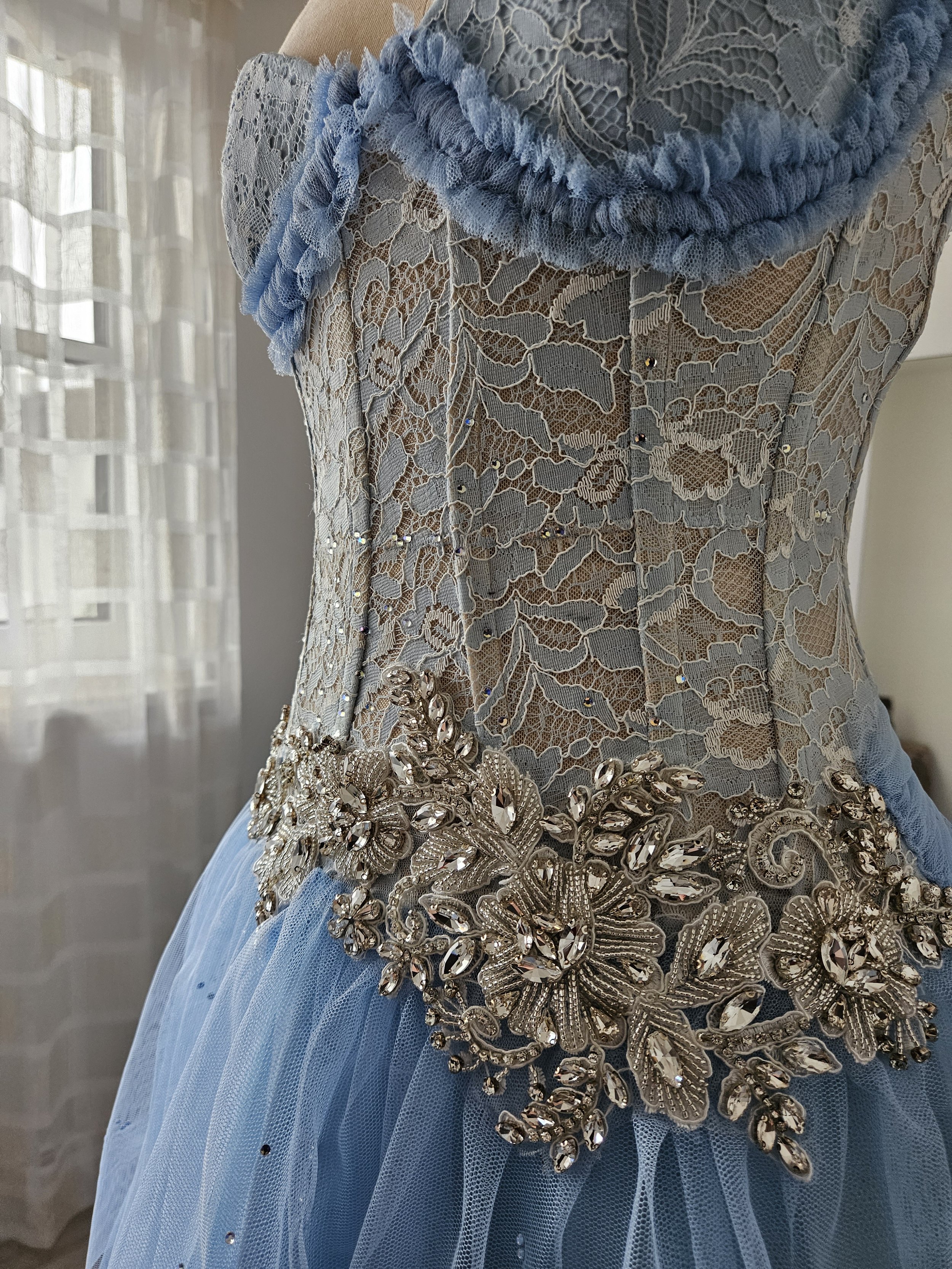 Detailaufnahme des Korsettoberteils eines pastellblauen Ballkleides aus transparenter Spitze, mit Tüll-Rüschen, Strass-Applikation in floralem Muster und Tüll-Rock.