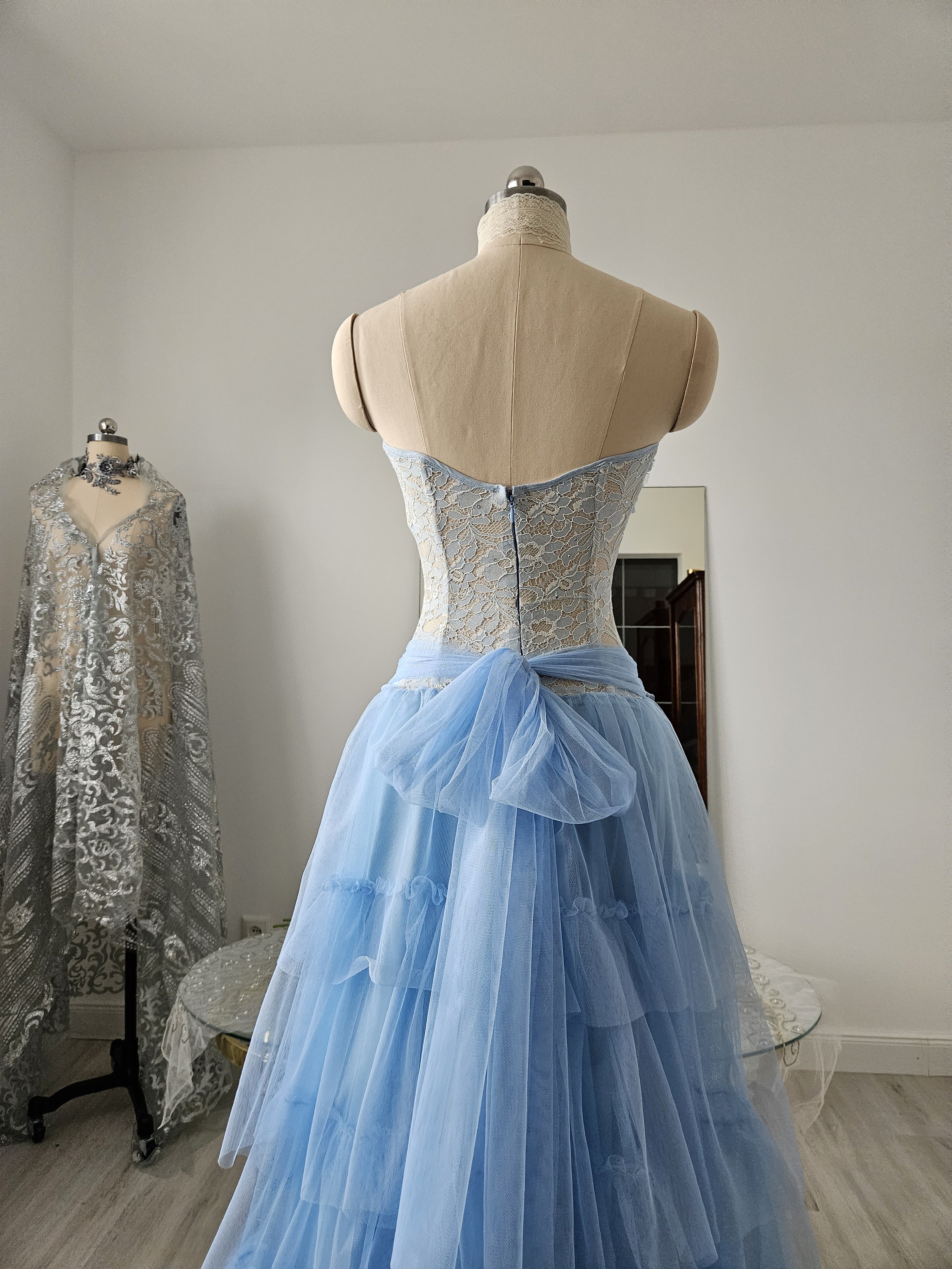 Rückansicht eines hellblauen Couture-Kleides in Korsettoptik aus floraler Spitze, mit Tüllband und Tüllrock im romantischen Theatrical Romantic-Stil. Handarbeit.