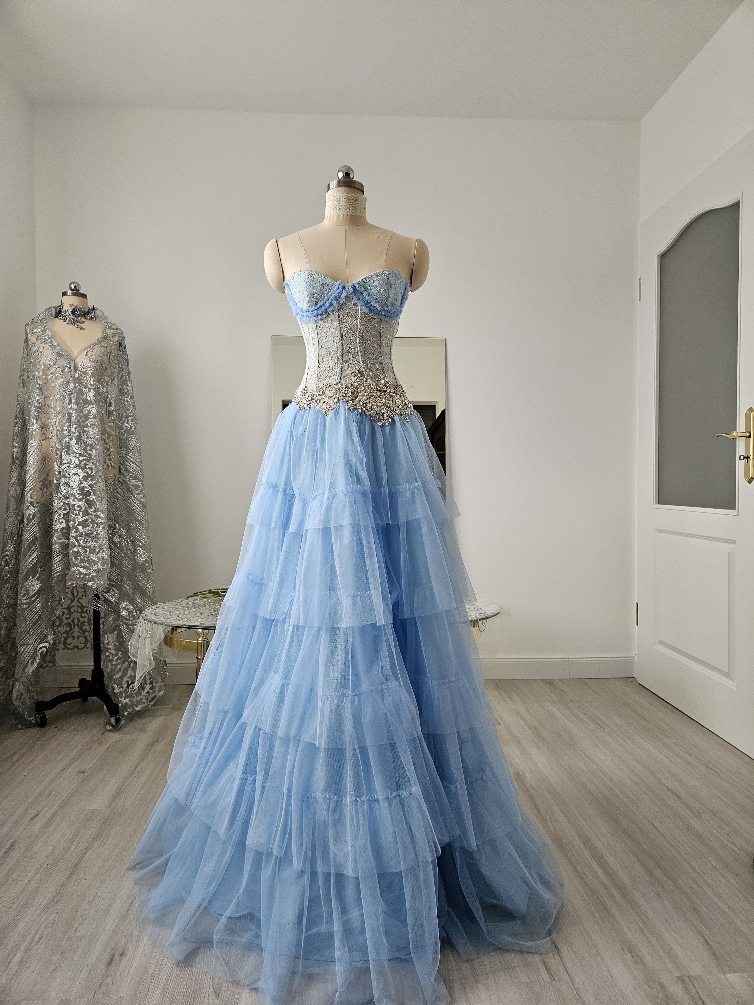 Korsettkleid aus Tüll und Spitze in hellblau / periwinkle, mit hochwertiger, glitzernder Brautkleidapplikation, mit ausladendem, abgestuftem Tüllrock in Bodenlänge. Couture-Kleid als Ballkleid.