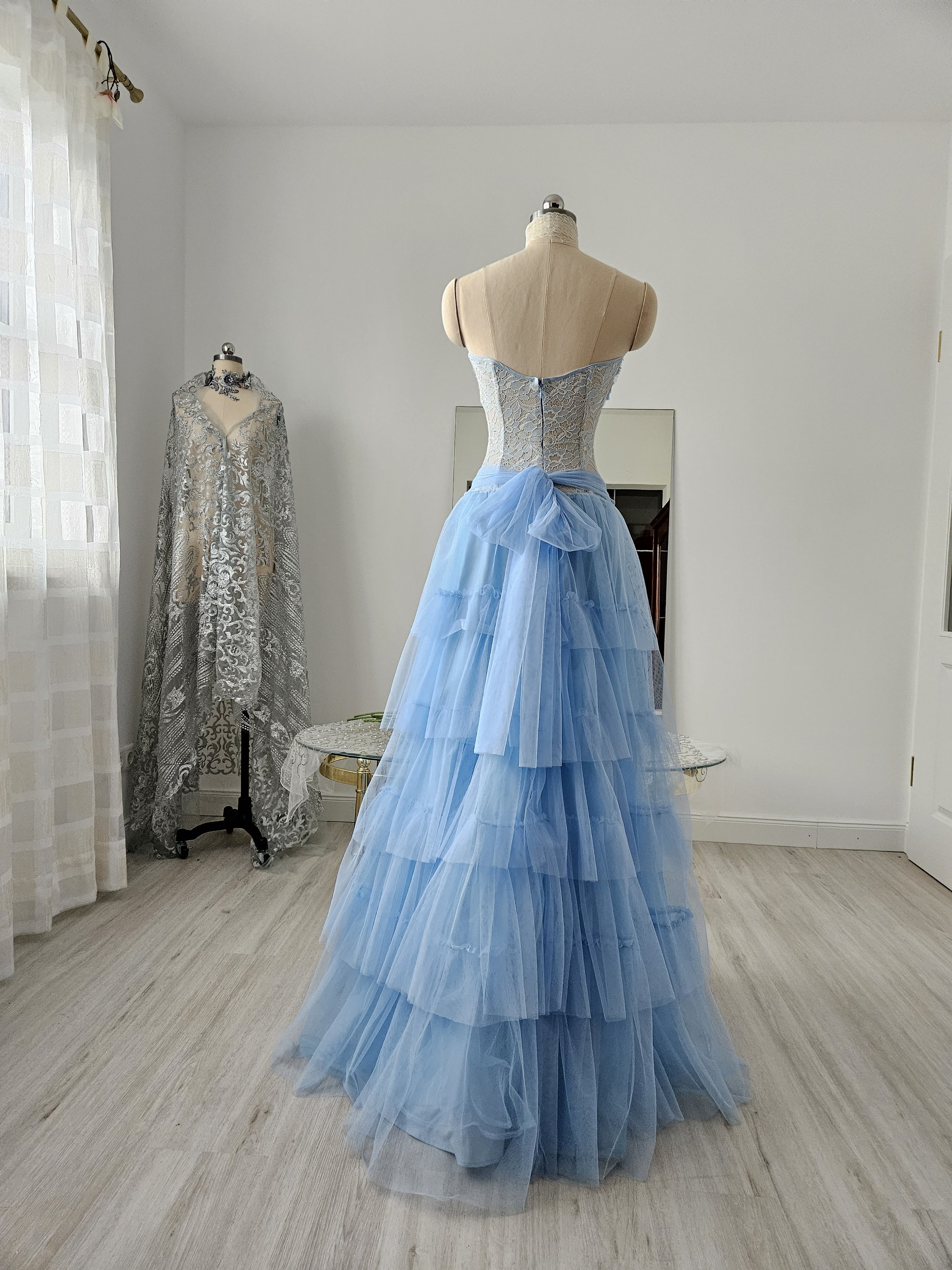 Rückansicht Korsettkleid in hellblau, mit bodenlangem, abgestuftem Rock aus leichtem Tüll und großer Schleife hinten, gefertigt aus feiner Spitze. Couture aus Deutschland