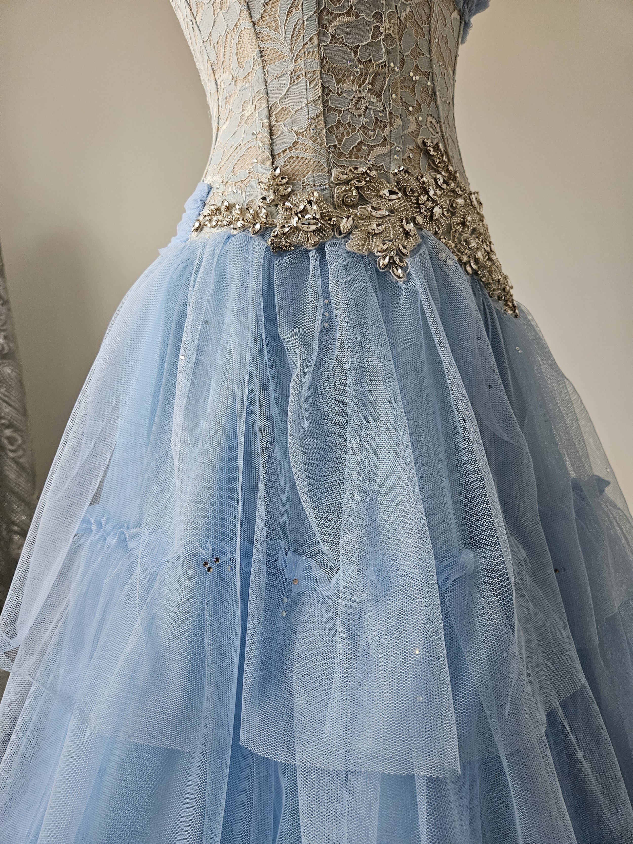 Detail-Aufnahme eines Korsettkleides aus transparenter Spitze in periwinkle mit Strasssteinen und floraler Glitzer-Applikation.