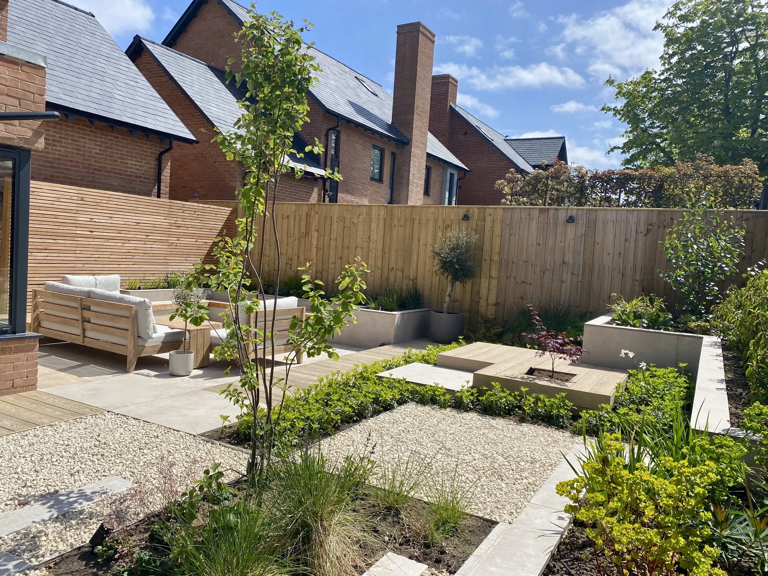 An image showing a view across a sunny garden to a corner seating area