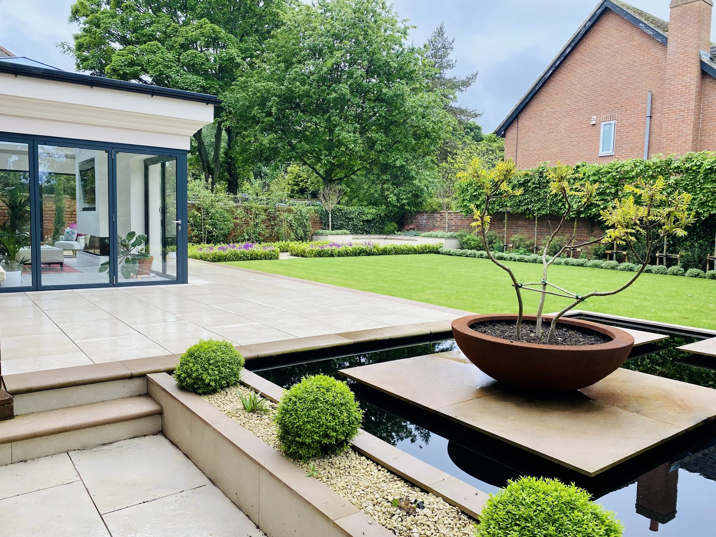 A photograph of the new garden with reflecting  pool, chipped topiary and feature planting in large contemporary plant pot