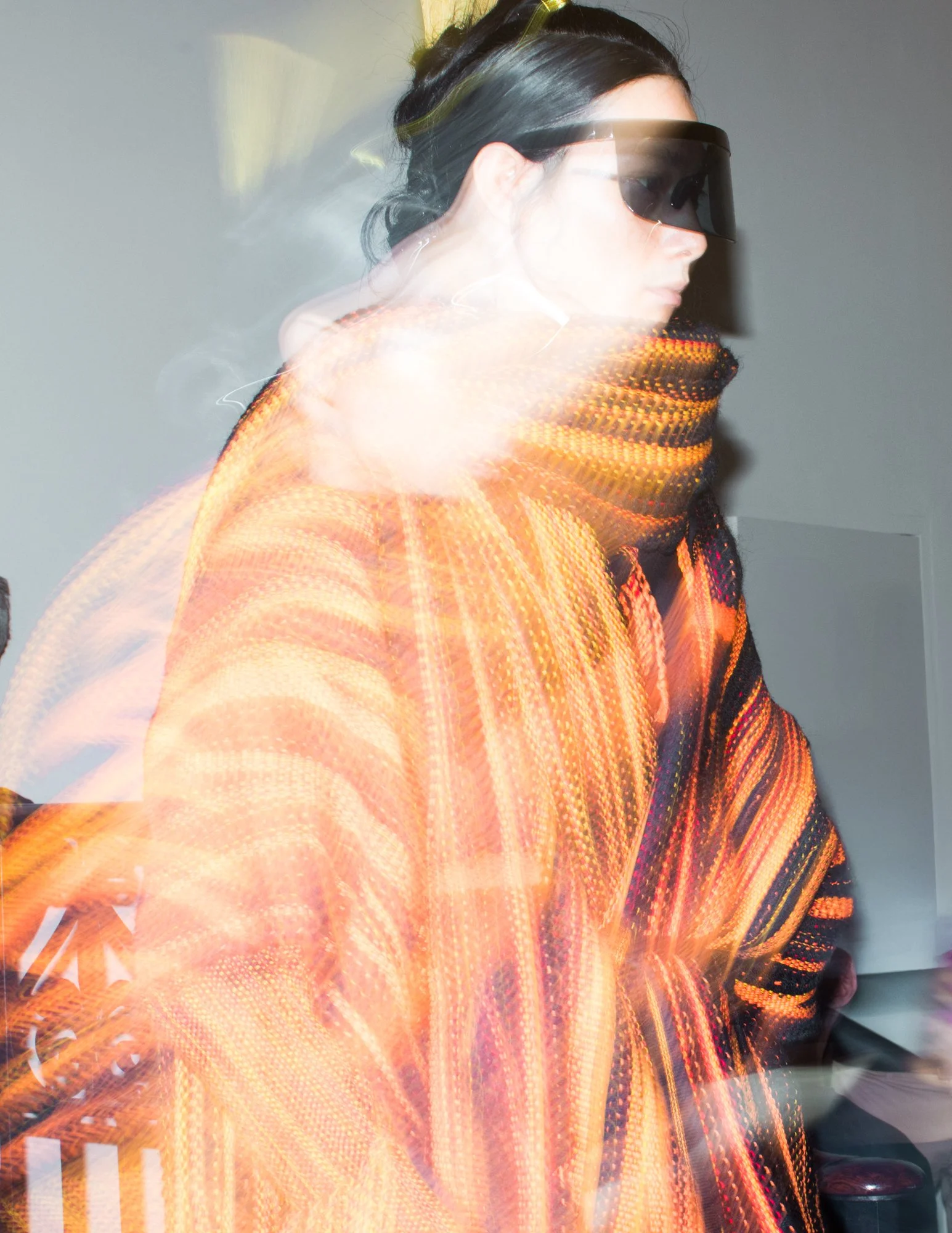 A woman wearing dark glasses and a multicolored orange and black sweater, with a motion-blur effect