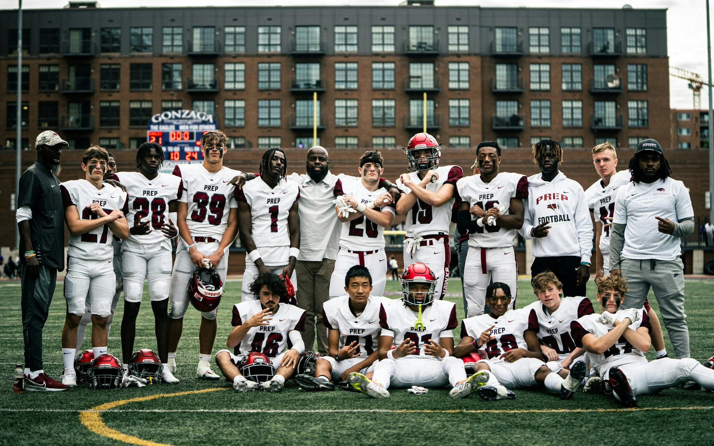 A group of football players and coaches standing on a football field after a game, with a scoreboard and city buildings in the background.