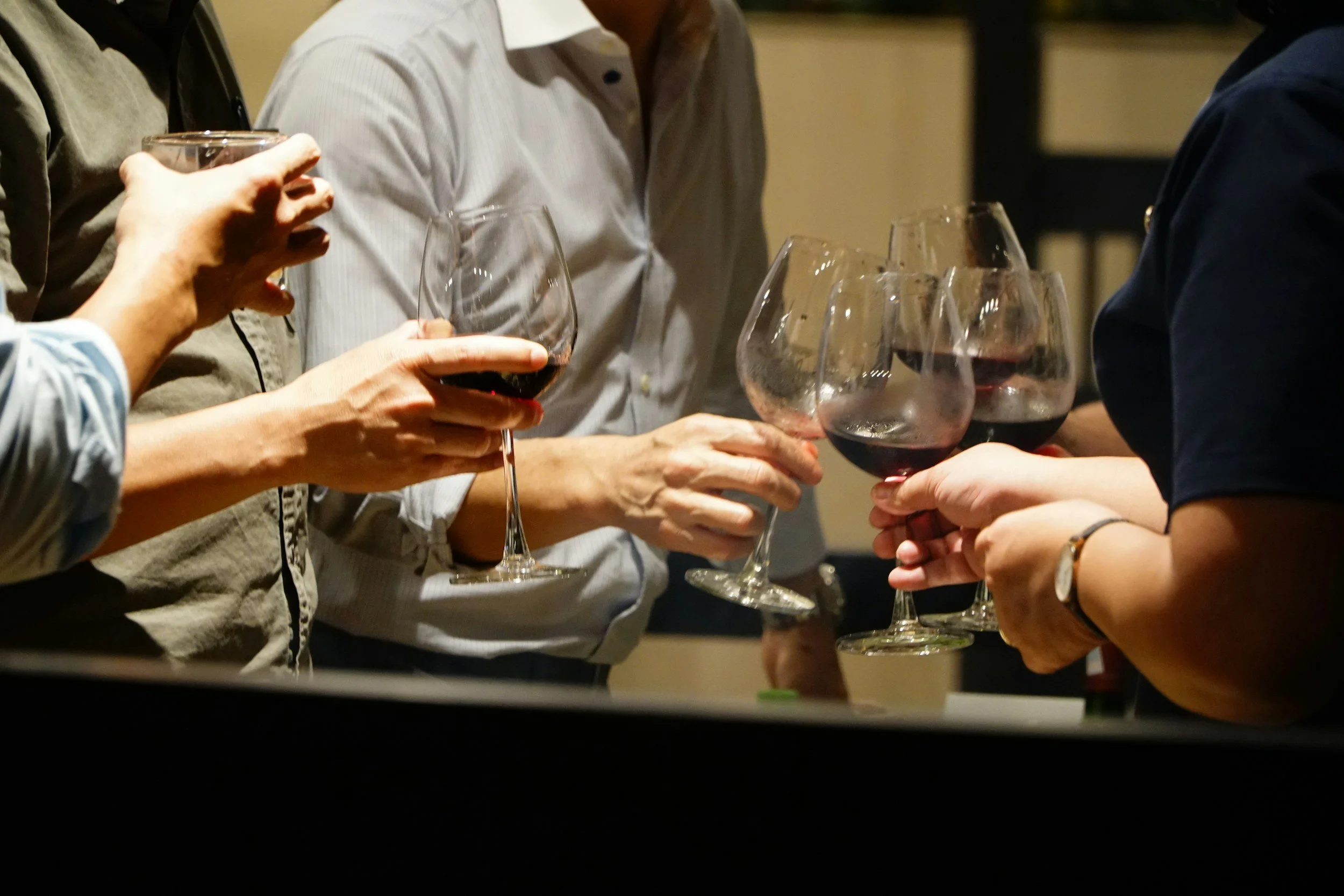 People holding glasses of red wine during a social gathering.