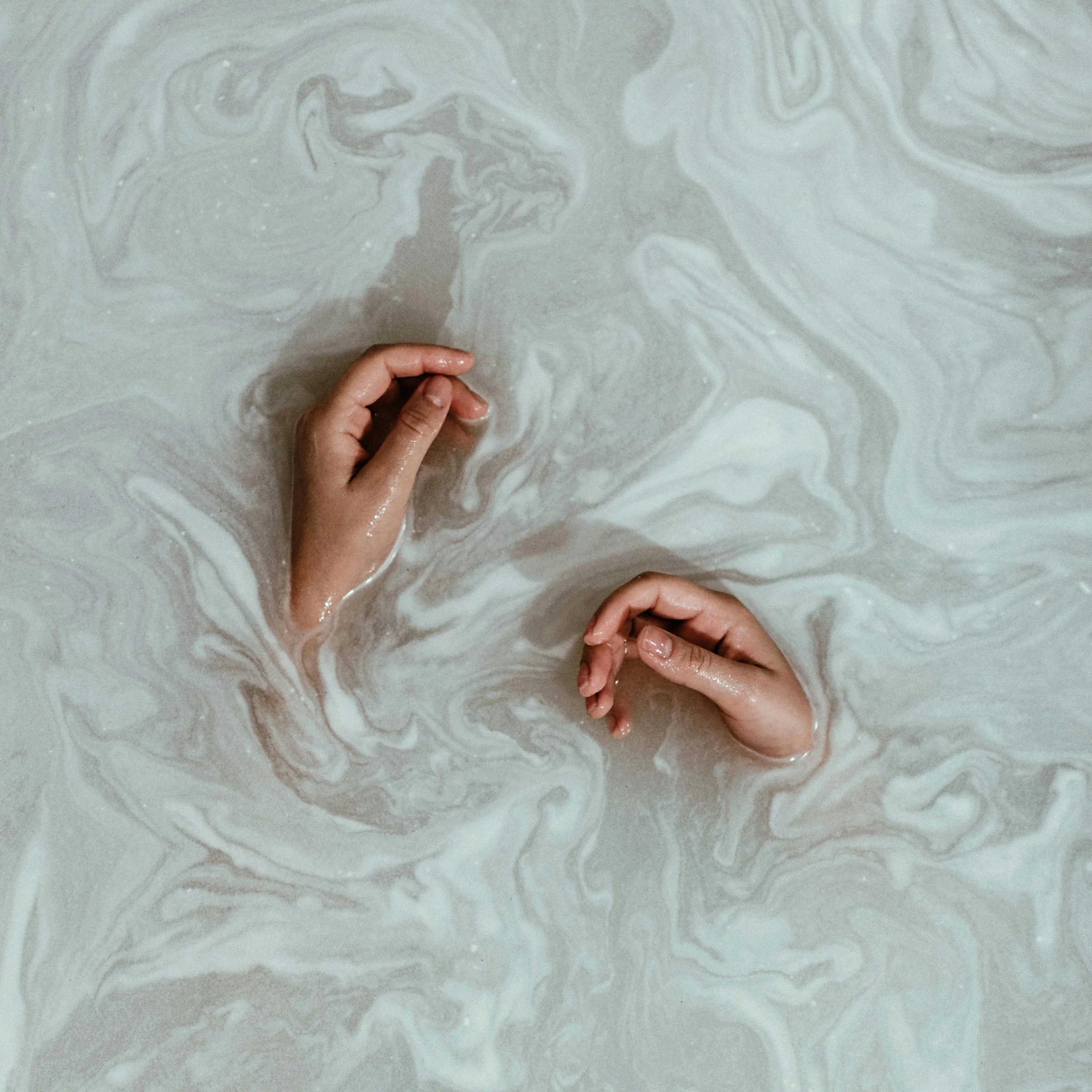 Two hands submerged in a swirling mixture of water and soap, creating a marbled effect.