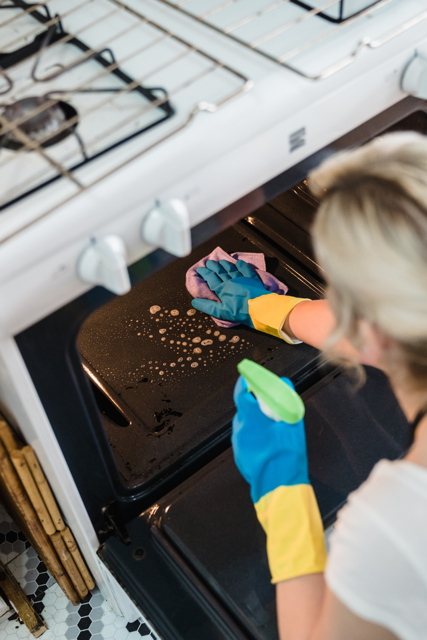 Person cleaning an oven with gloves and a spray bottle
