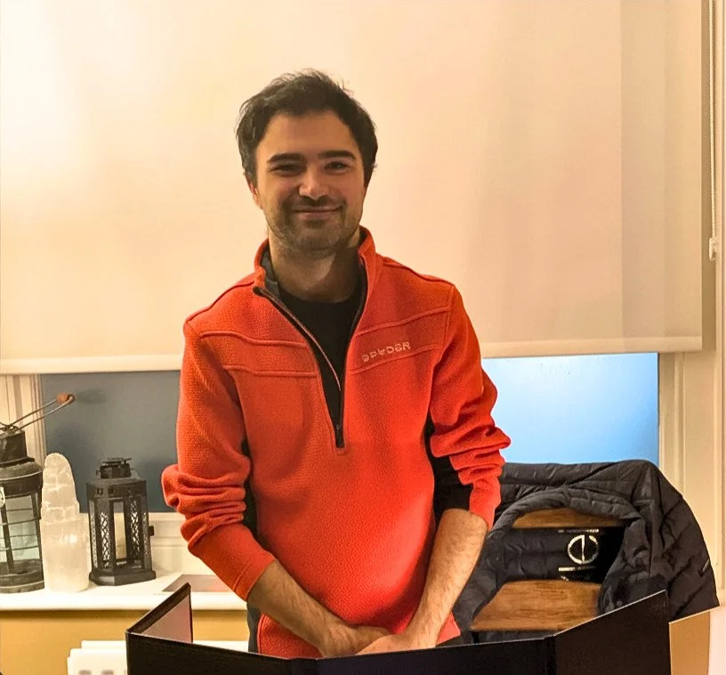 A man wearing an orange jumper stands smiling behind a DM screen.