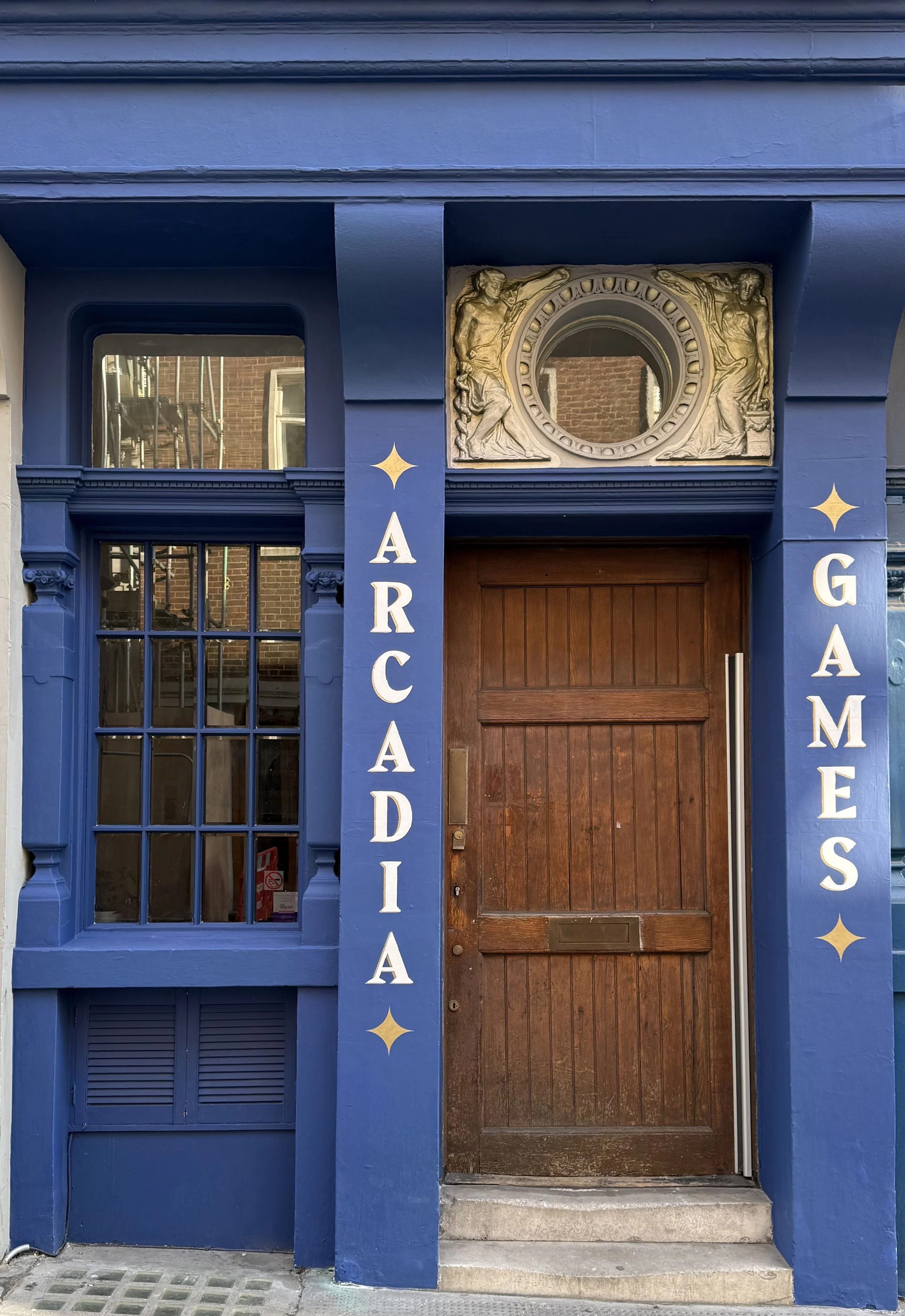 Blue painted facade of an arcade and games shop with a wooden door, window, and decorative sculptures above the entrance.