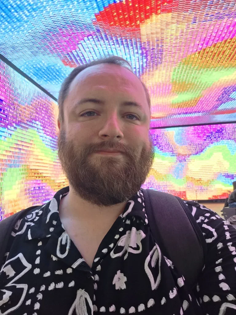 A bearded human standing inside a rainbow cube.