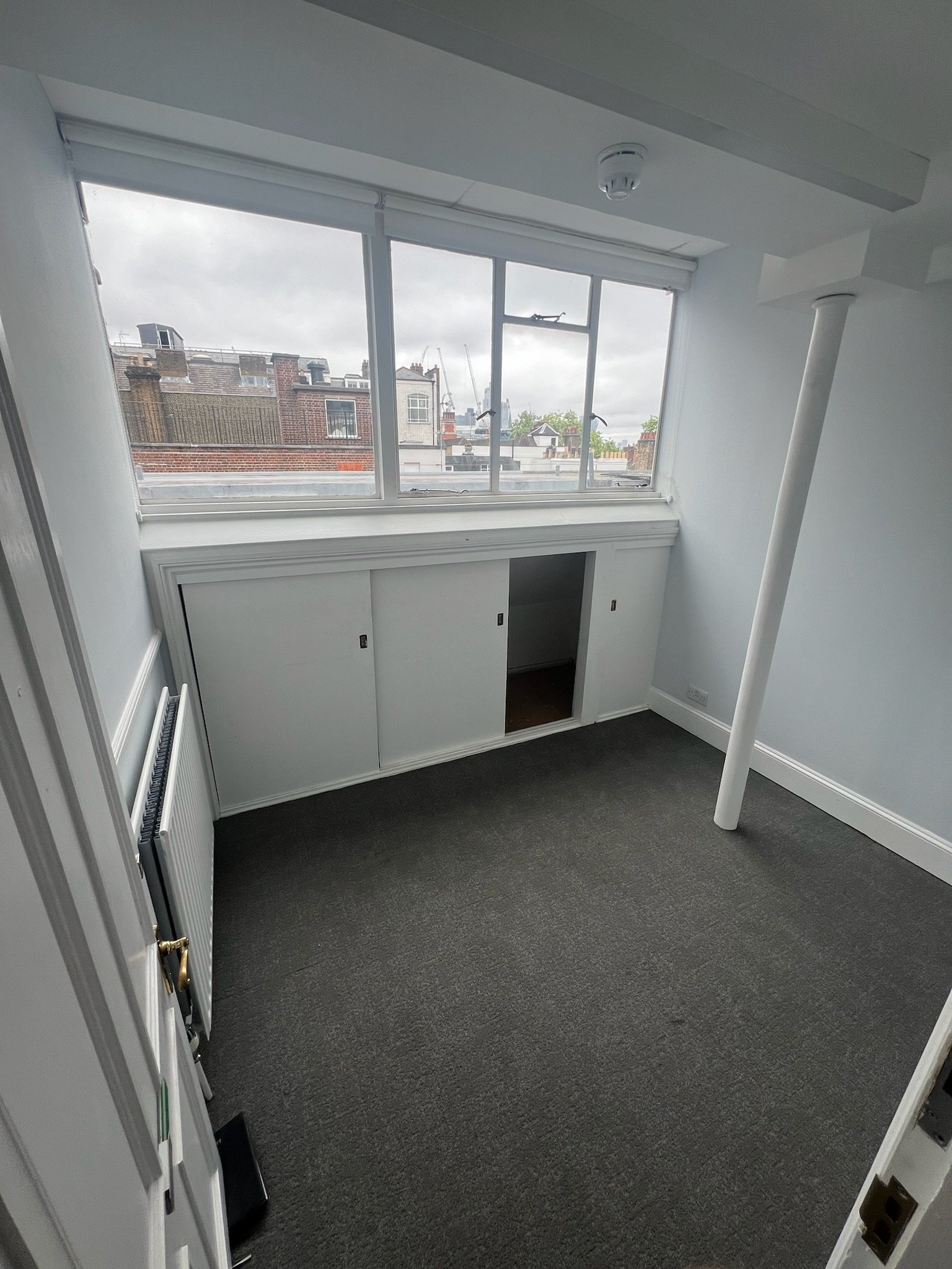 Empty room with gray carpet, white walls, a large window with city view, and built-in white cabinets.