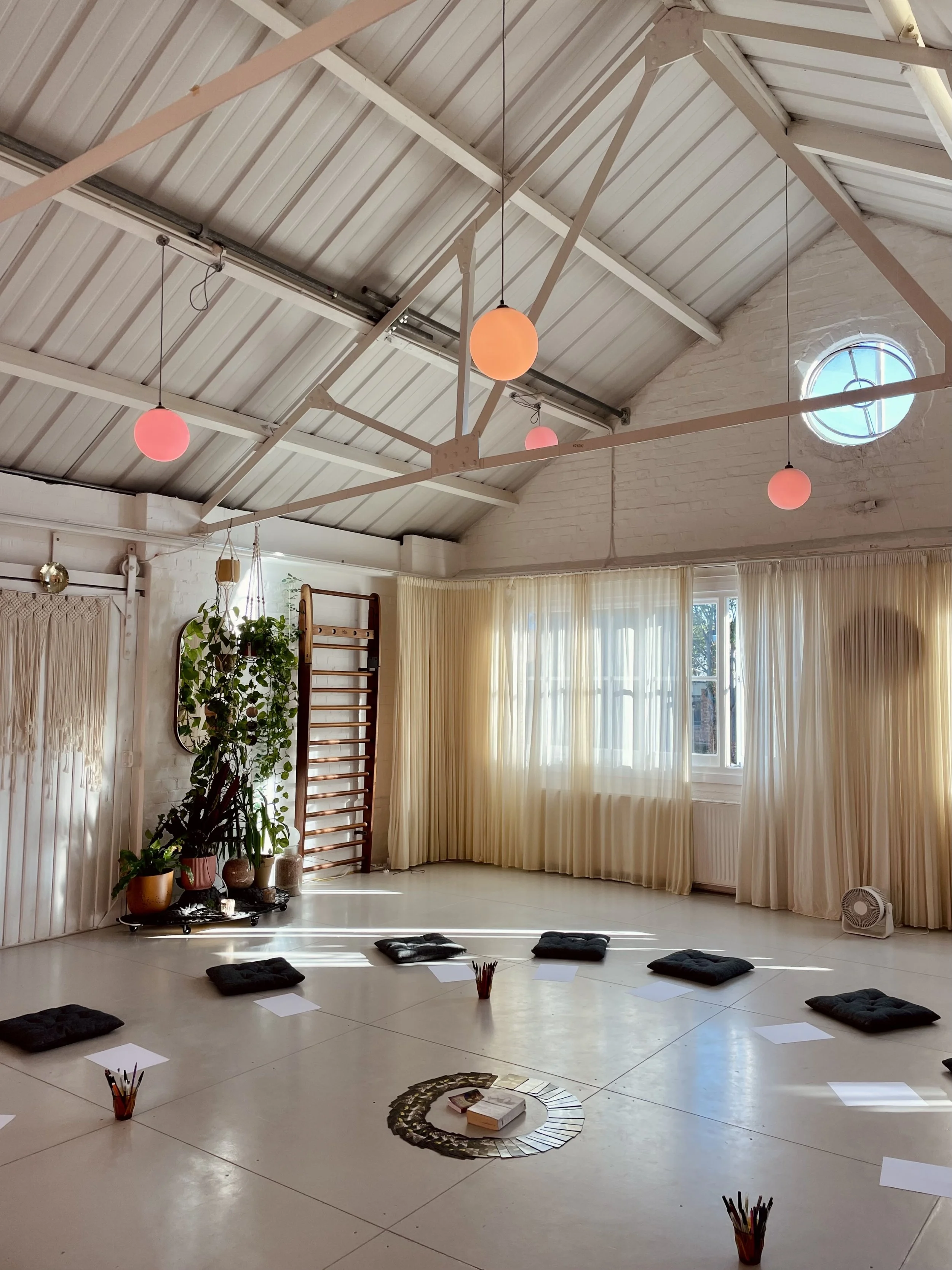 Living room with large windows, outdoor fire pit, string lights, colorful pillows on the floor, and several patterned area rugs.