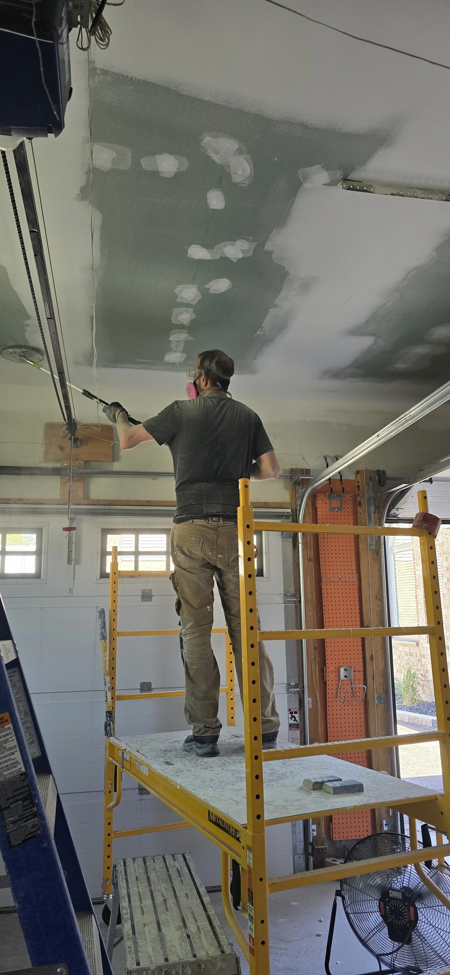Image shows Steve Peckham, business owner, sanding drywall seams on mositure resistant and fire code drywall and preparing ceiling to be painted