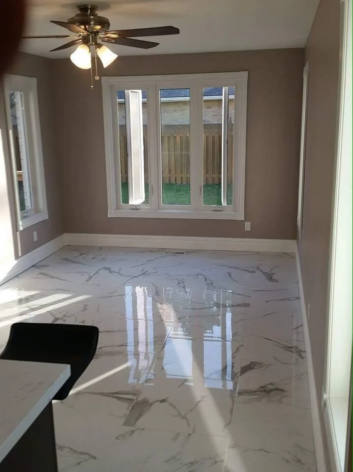 Empty room with beige walls, large window, marble floor, ceiling fan with lights, and a black chair partially visible.