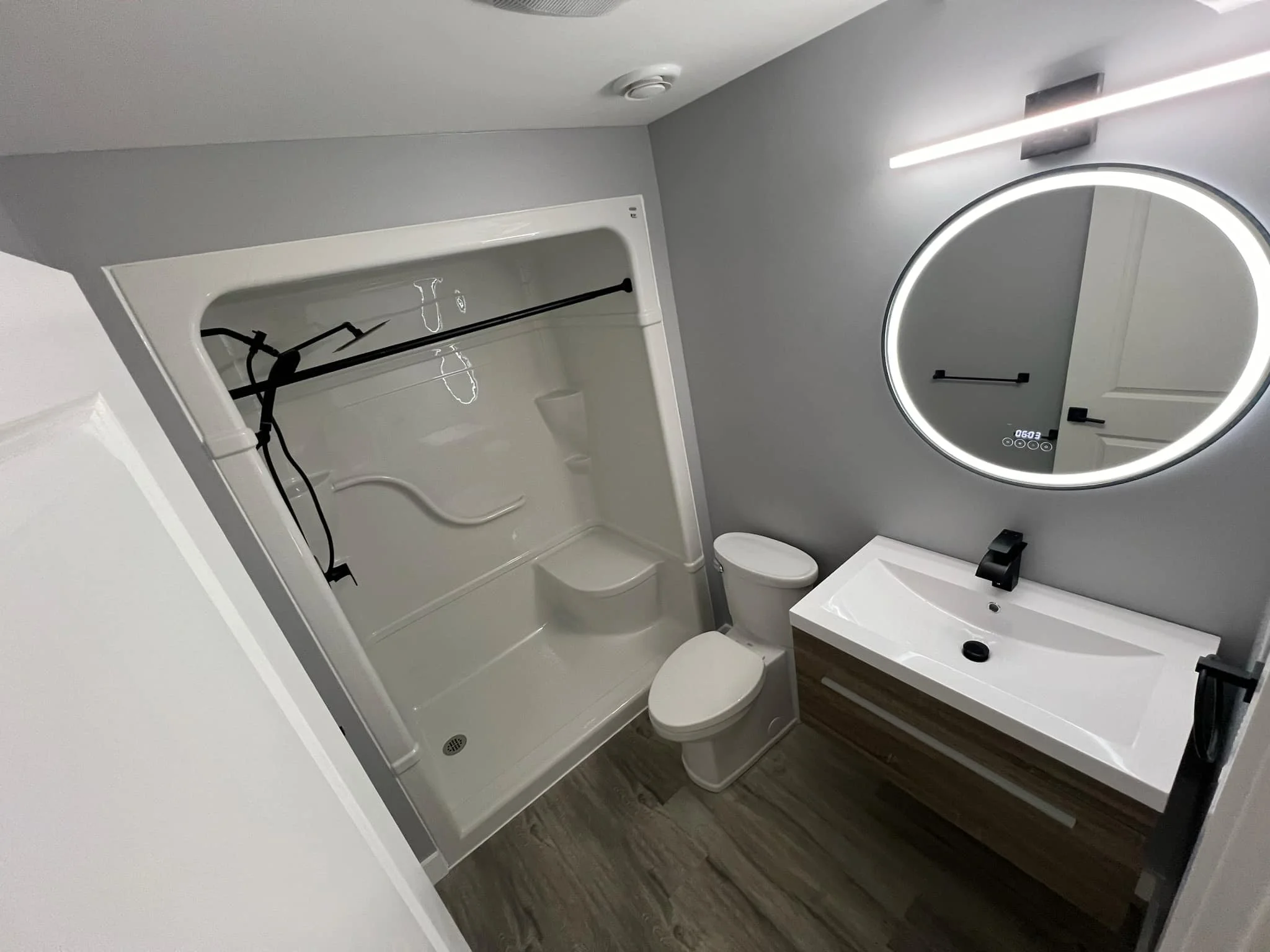 Accessible bathroom with walk-in bathtub, floating vanity, round LED mirror, and matte black fixtures.