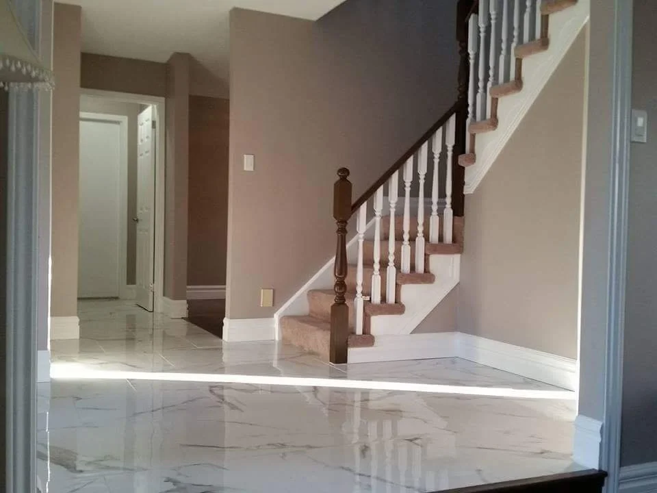 Interior view of a house with beige walls, marble flooring, and a staircase with wooden steps and white spindles.
