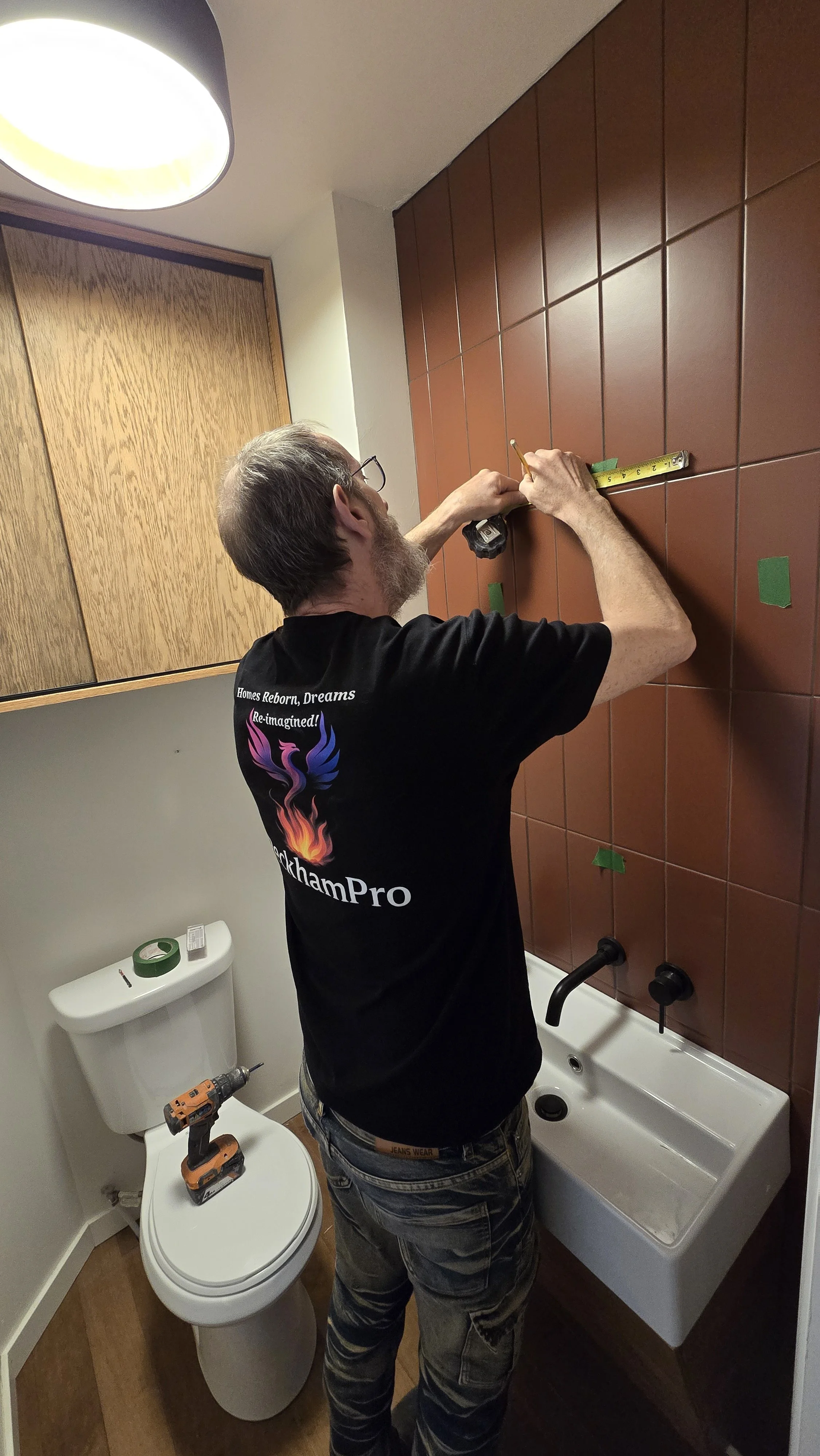 Contractor installing  custom oak cabinetry, floating sink and wall terra-cotta tile feature wall during a professional bathroom renovation.