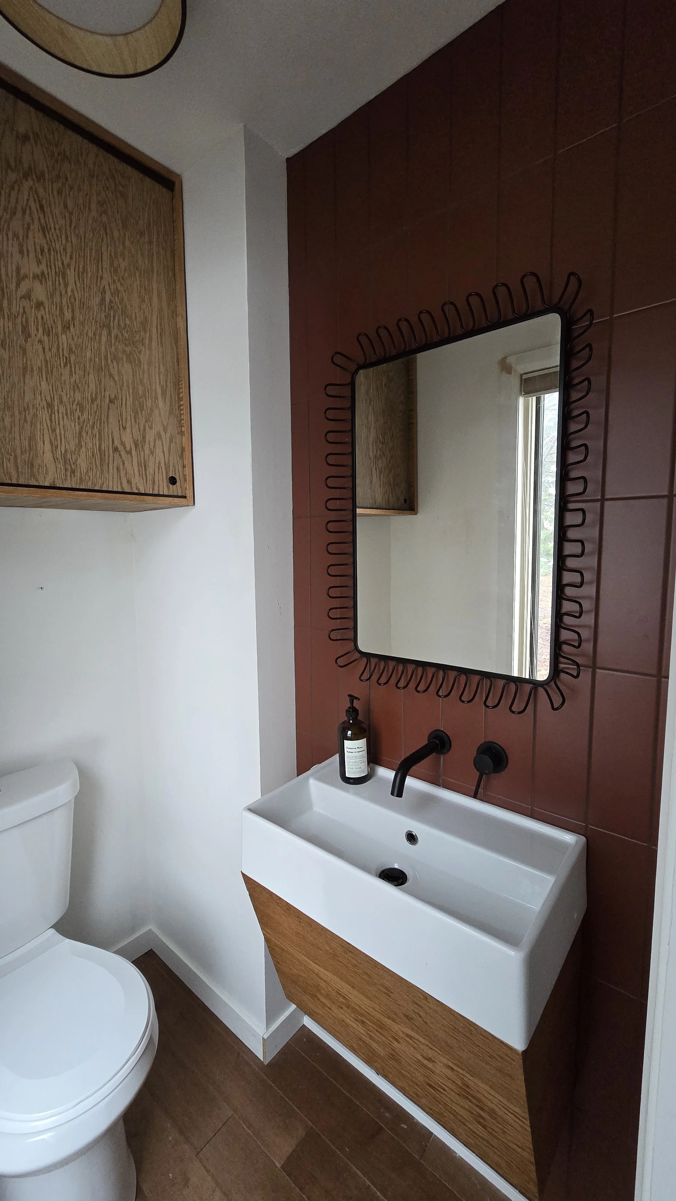 Modern bathroom with warm wood custom cabinets, floating vanity, vessel sink, and decorative framed mirror.