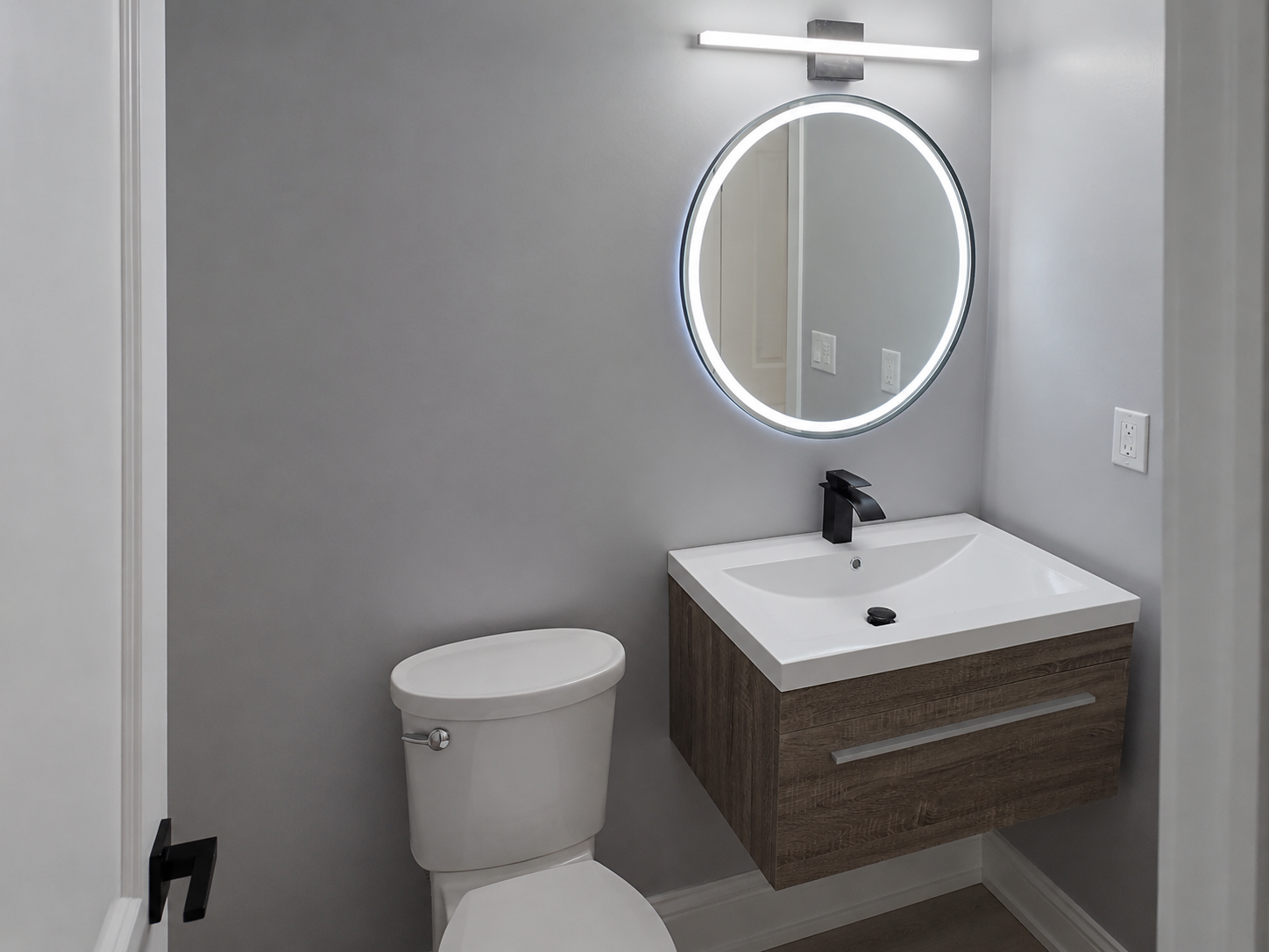 Compact bathroom with floating vanity, round LED mirror, matte black fixtures, and contemporary design.