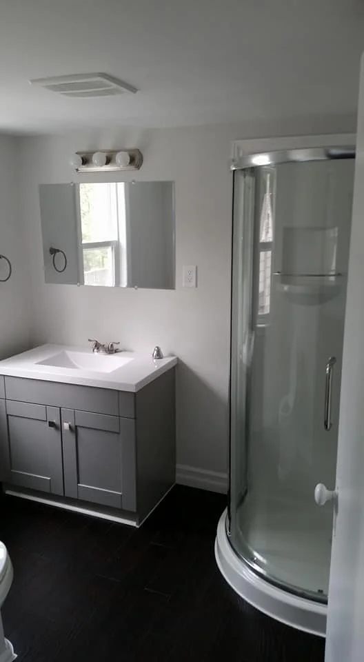 Bathroom featuring a corner glass shower, grey vanity with quartz countertop, and contemporary lighting.