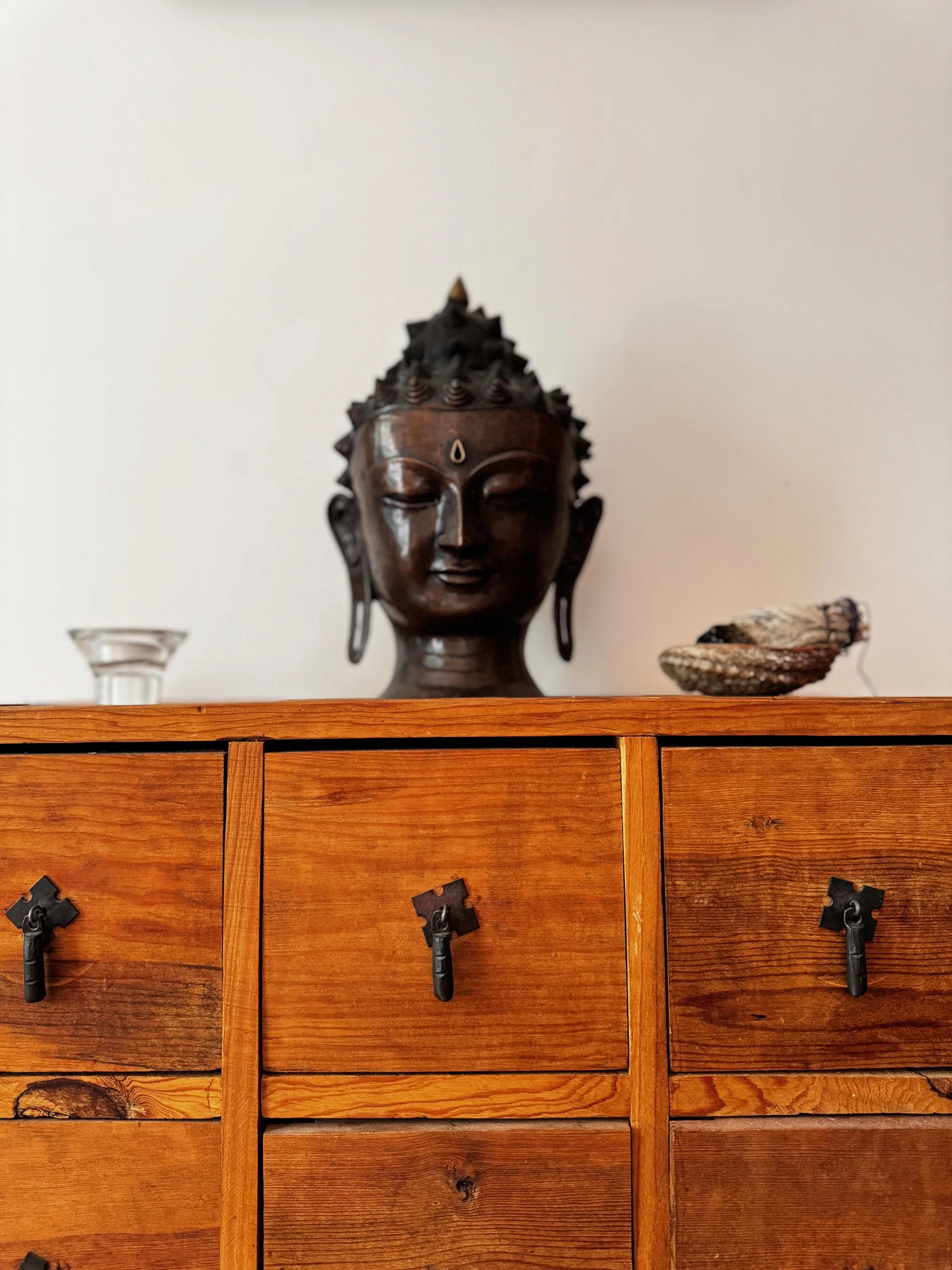 Wooden chest of drawers with a Buddha head sculpture and small decorative items on top.