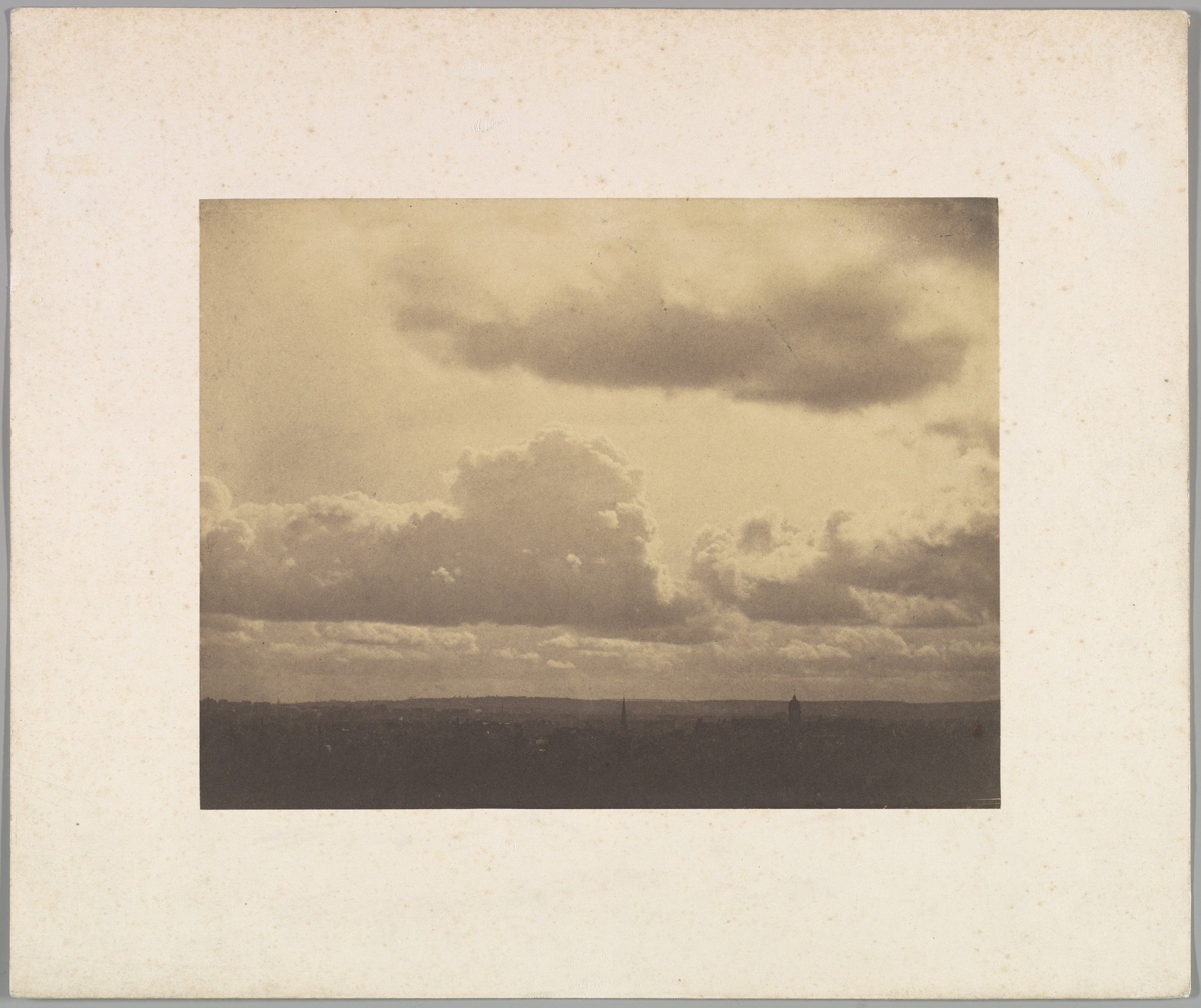 Sepia-toned photograph of sky with dramatic clouds over a distant landscape.