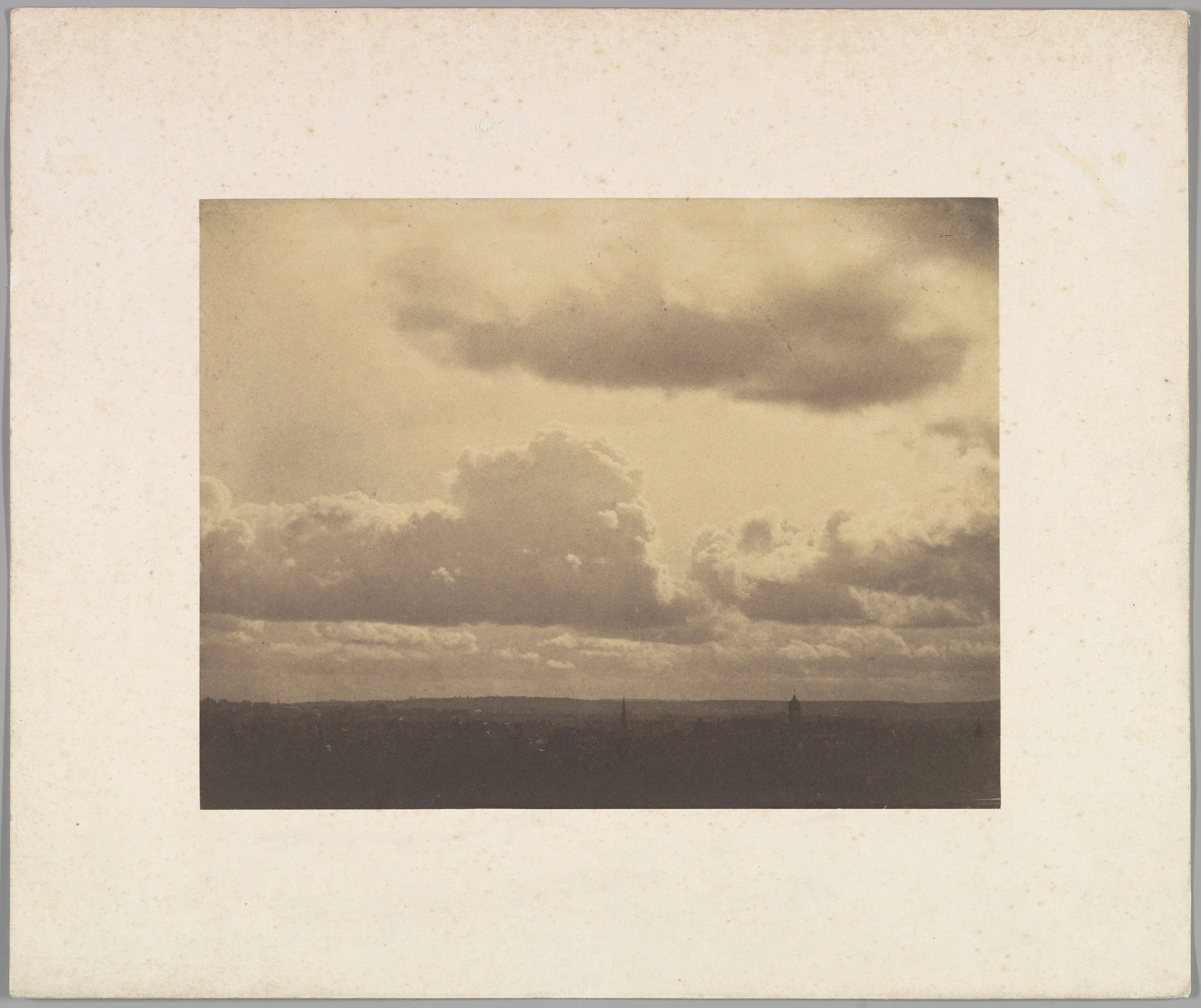 Sepia-toned photograph of sky with dramatic clouds over a distant landscape.