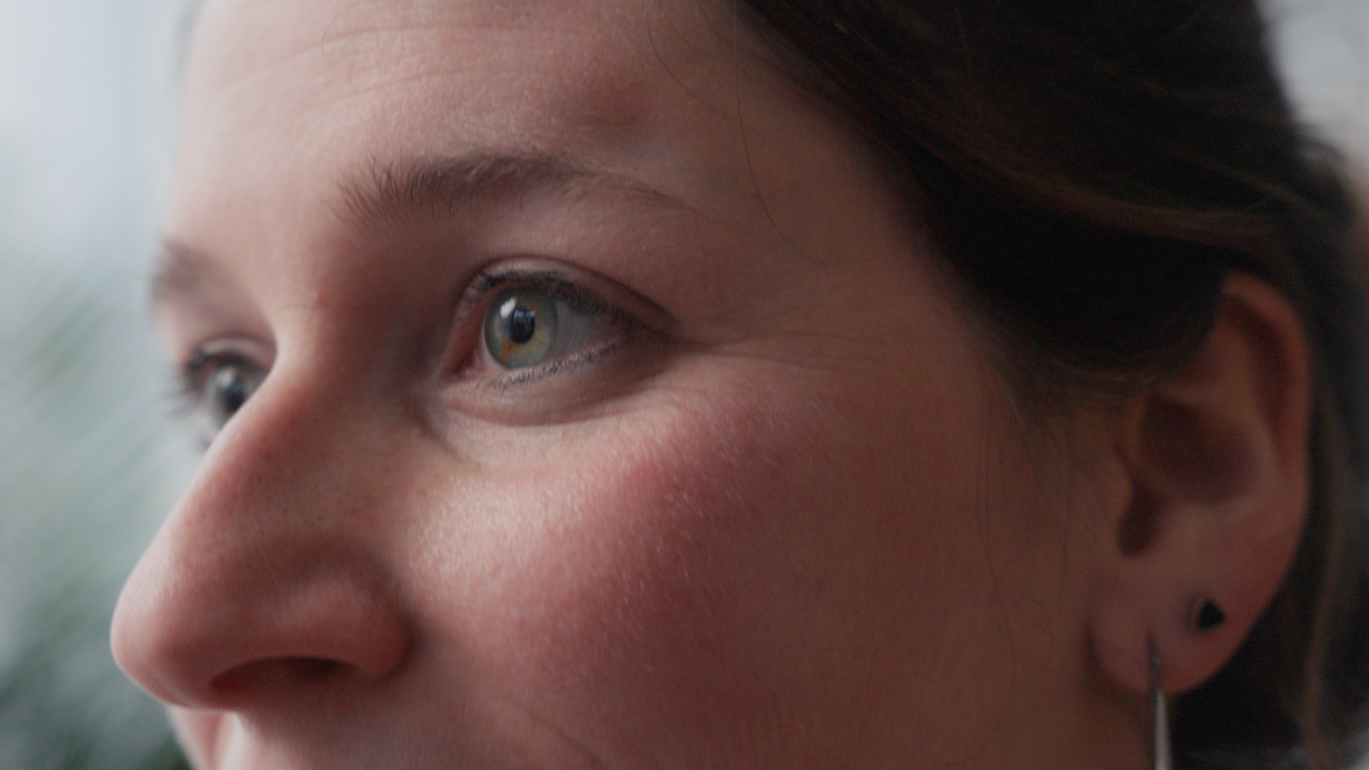 Close-up of a person's face, showing the right eye and part of the nose, with light skin and dark brown hair, looking out of focus to the left.