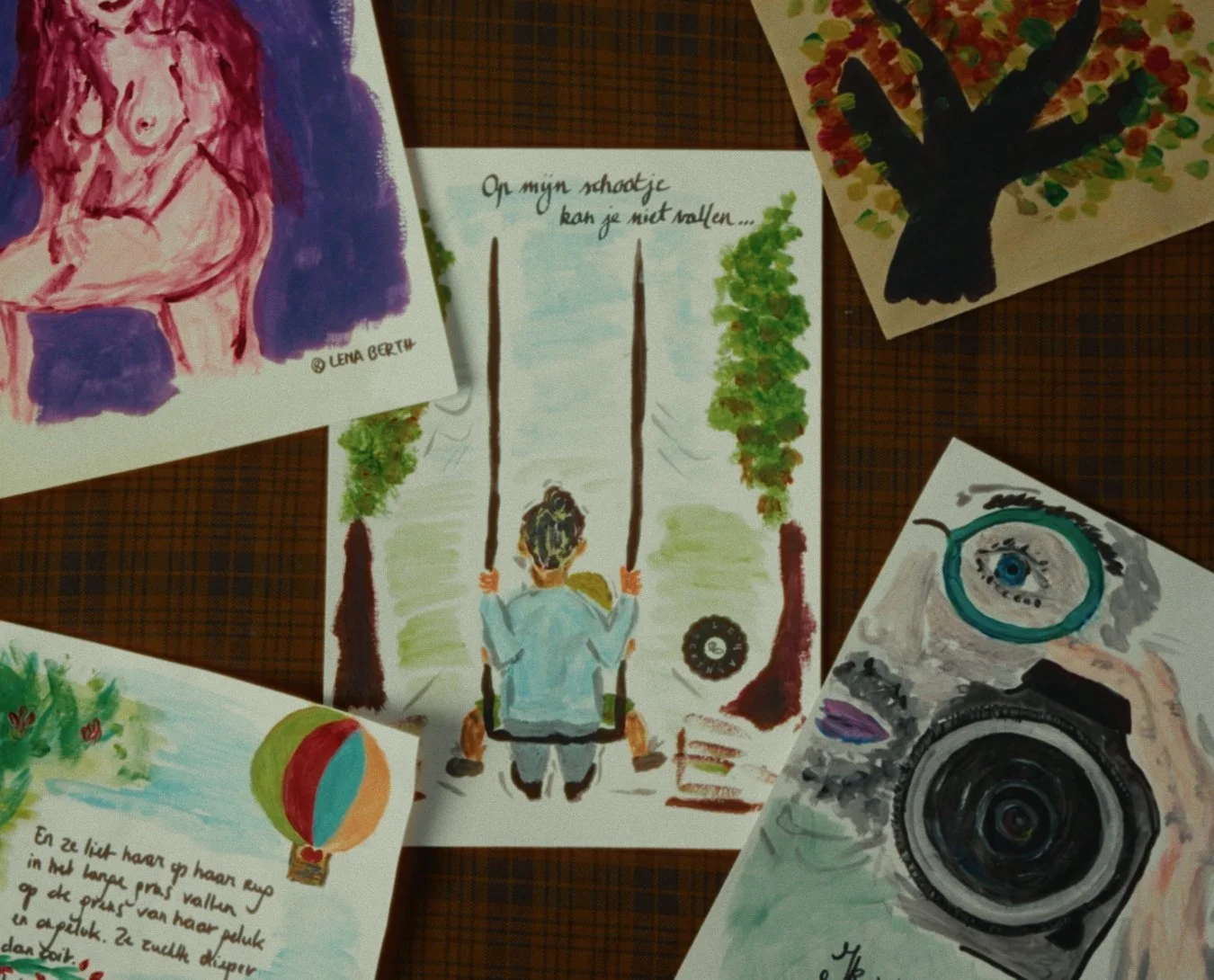 Collection of five watercolor paintings on paper, including a woman with a child on a swing, a tree with colorful leaves, a portrait of an eye and camera, a hot air balloon, and a person sitting on grass. Some paintings include handwritten notes in Dutch.