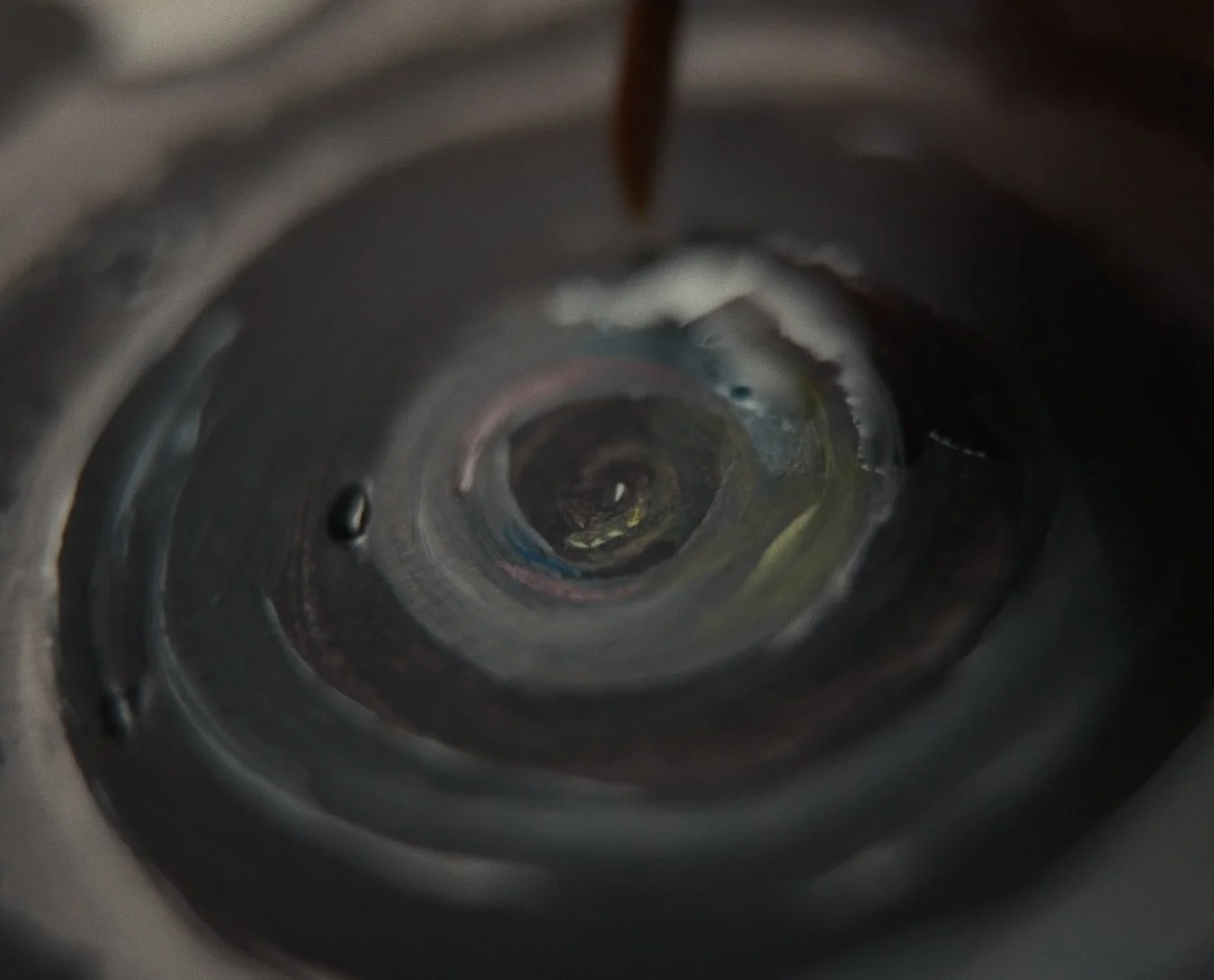 The image shows the inside of a metallic cylindrical container with liquid pouring into it from above, possibly a pipe or spout, with a dark background.