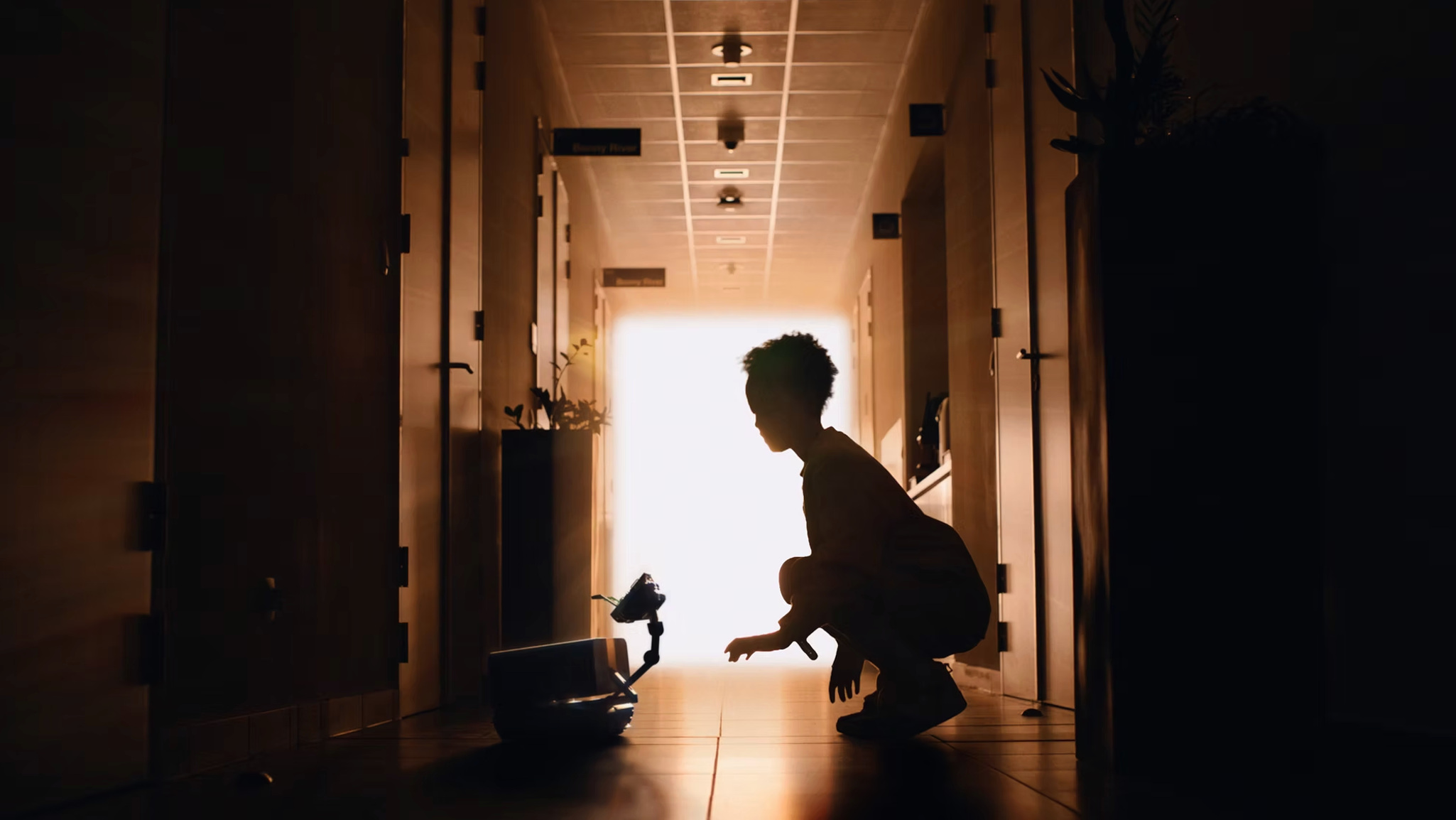 Silhouette of a person sitting in a hallway backlit by bright light, with plants on the side.
