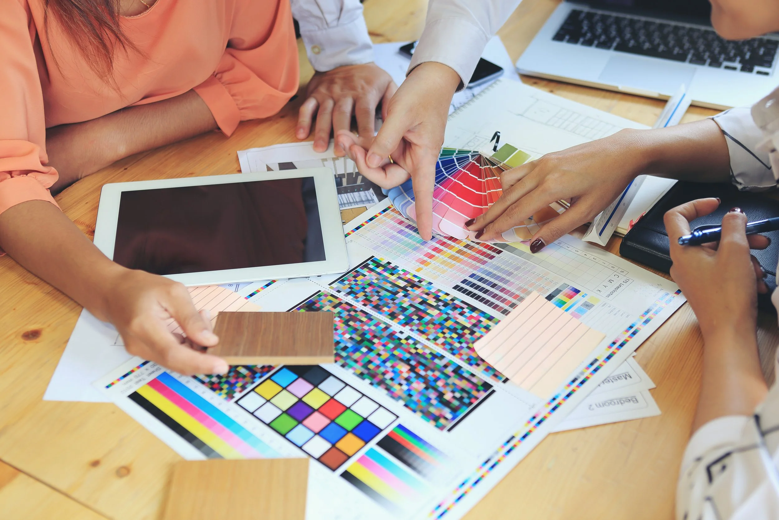 People discussing color schemes, with color swatches, palettes, and a tablet on a wooden table.