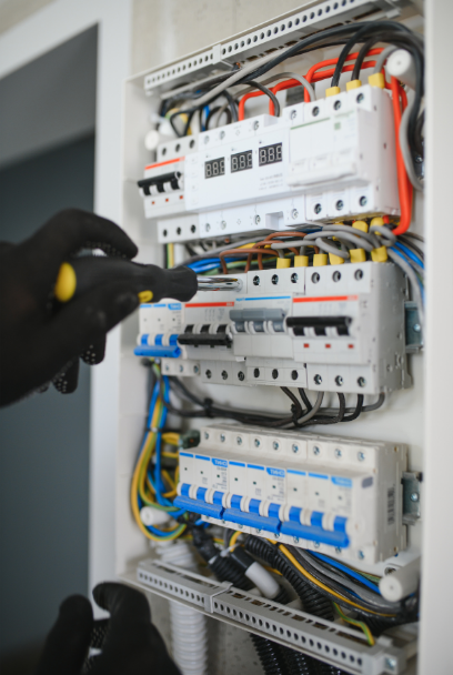 Personne manipulant un tableau électrique avec des disjoncteurs et des câbles de différentes couleurs.