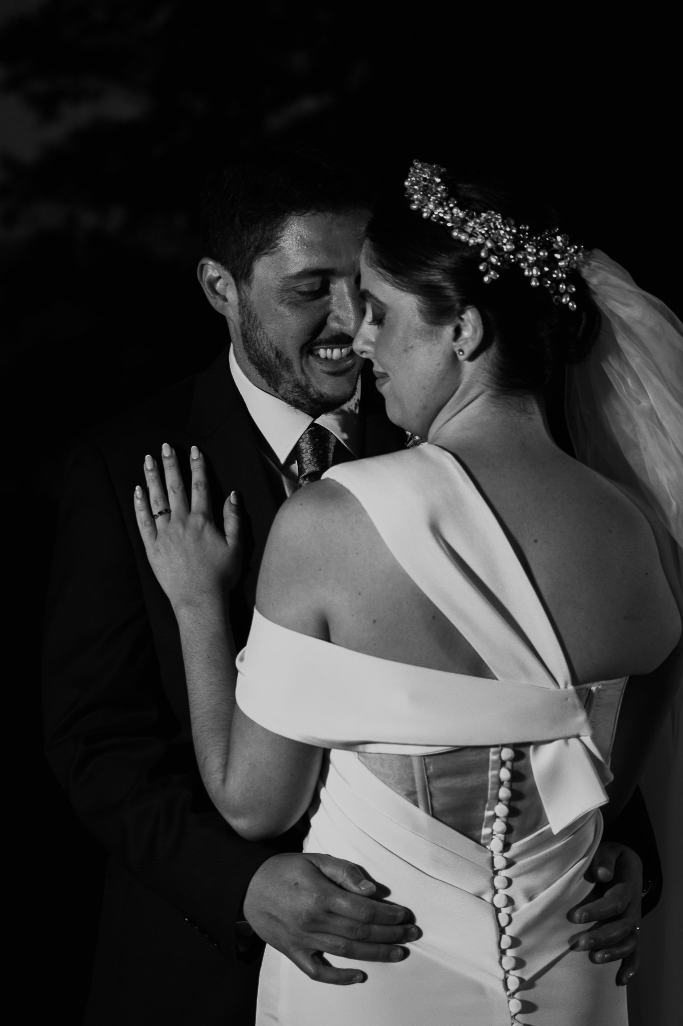 Pareja de novios abrazados en su boda, él con traje y ella con vestido de novia, en una foto en blanco y negro.