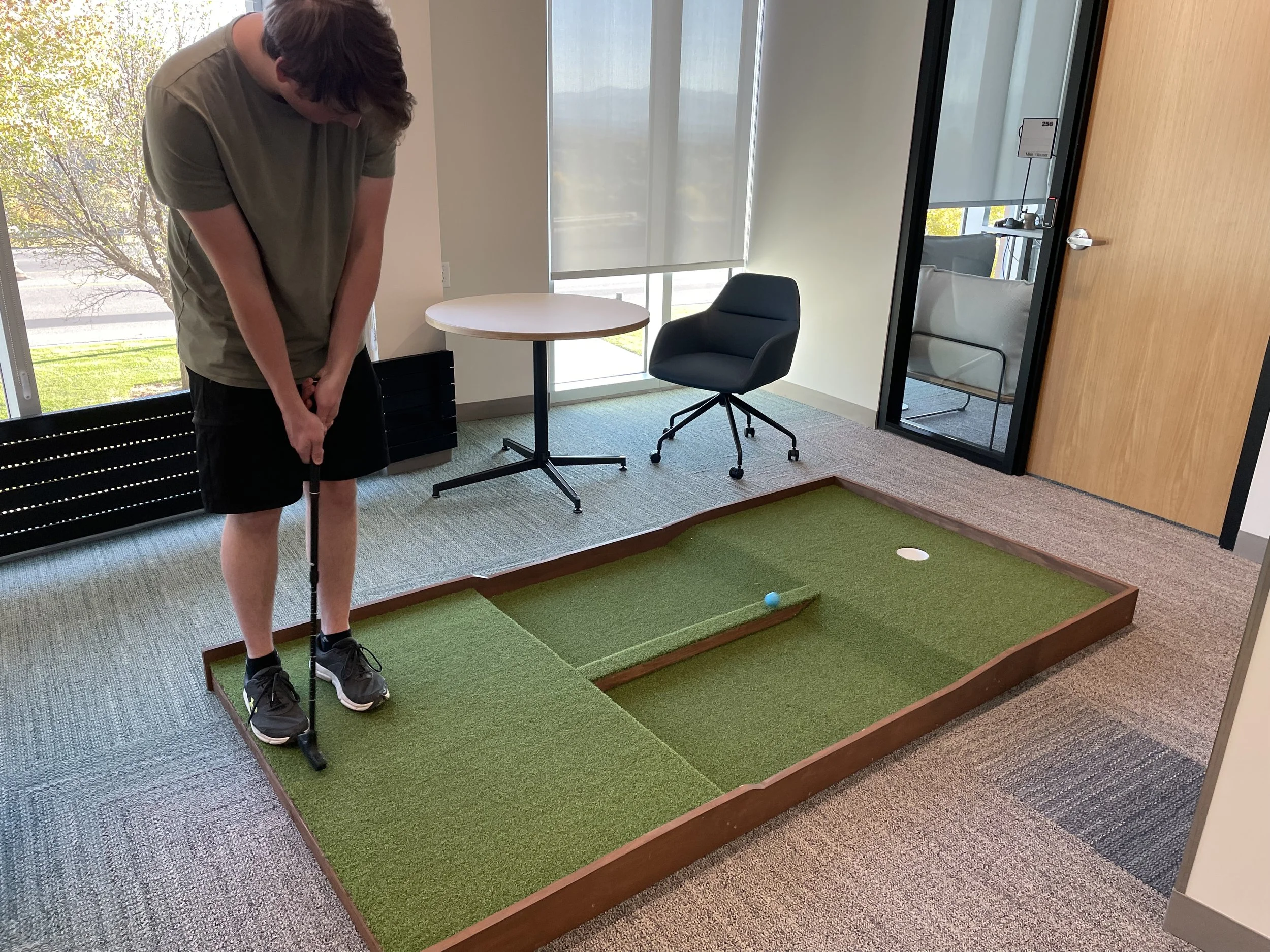 Person playing indoor mini golf on a small, raised putting green with a blue ball and a hole.