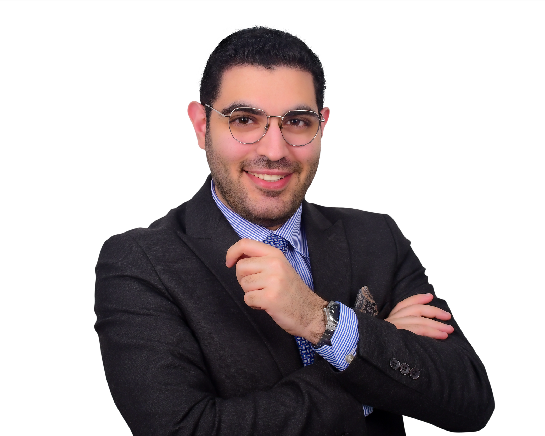 A man with dark hair, wearing glasses, a black blazer, and a blue striped shirt, smiling and crossing his arms, with a watch on his left wrist.