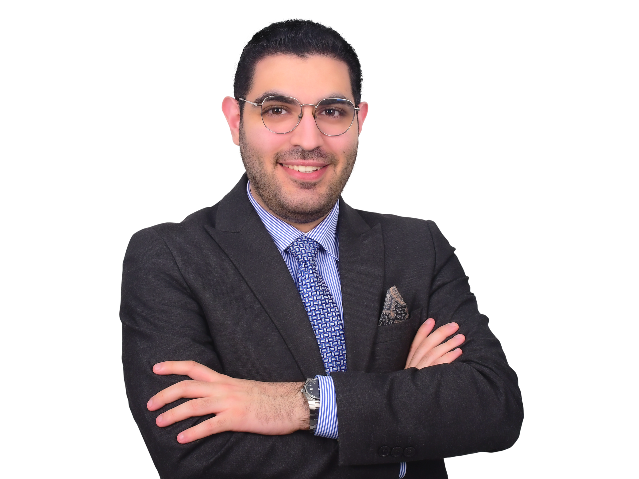 A man wearing glasses, a dark suit, a blue striped shirt, and a patterned tie, smiling with arms crossed.