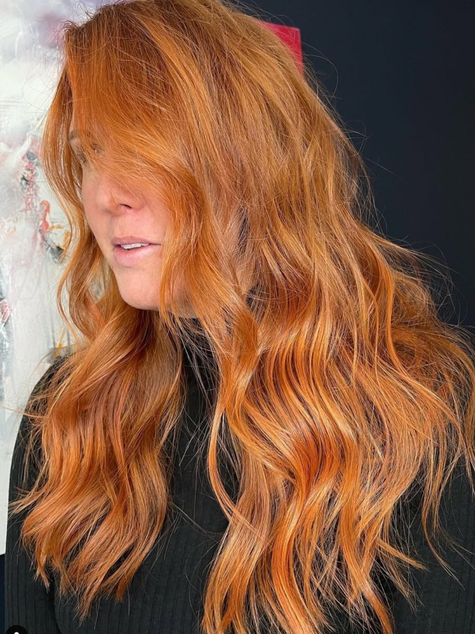 Close-up of a person with long, wavy red hair, wearing a black top.