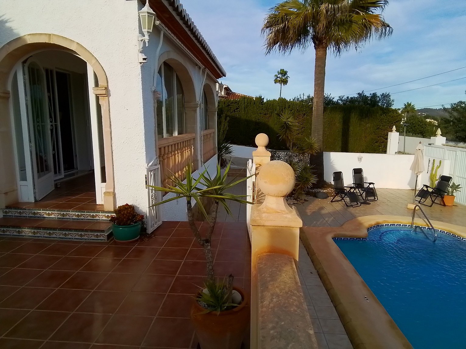 Mediterranean-style villa with pool and patio, surrounded by palm trees and pot plants.