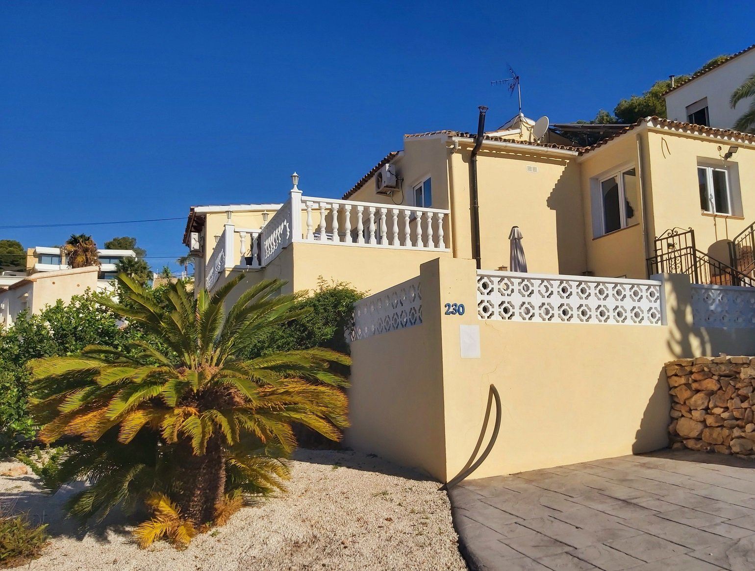 Mediterranean-style house with cream exterior, decorative balustrade, and palm tree in foreground.