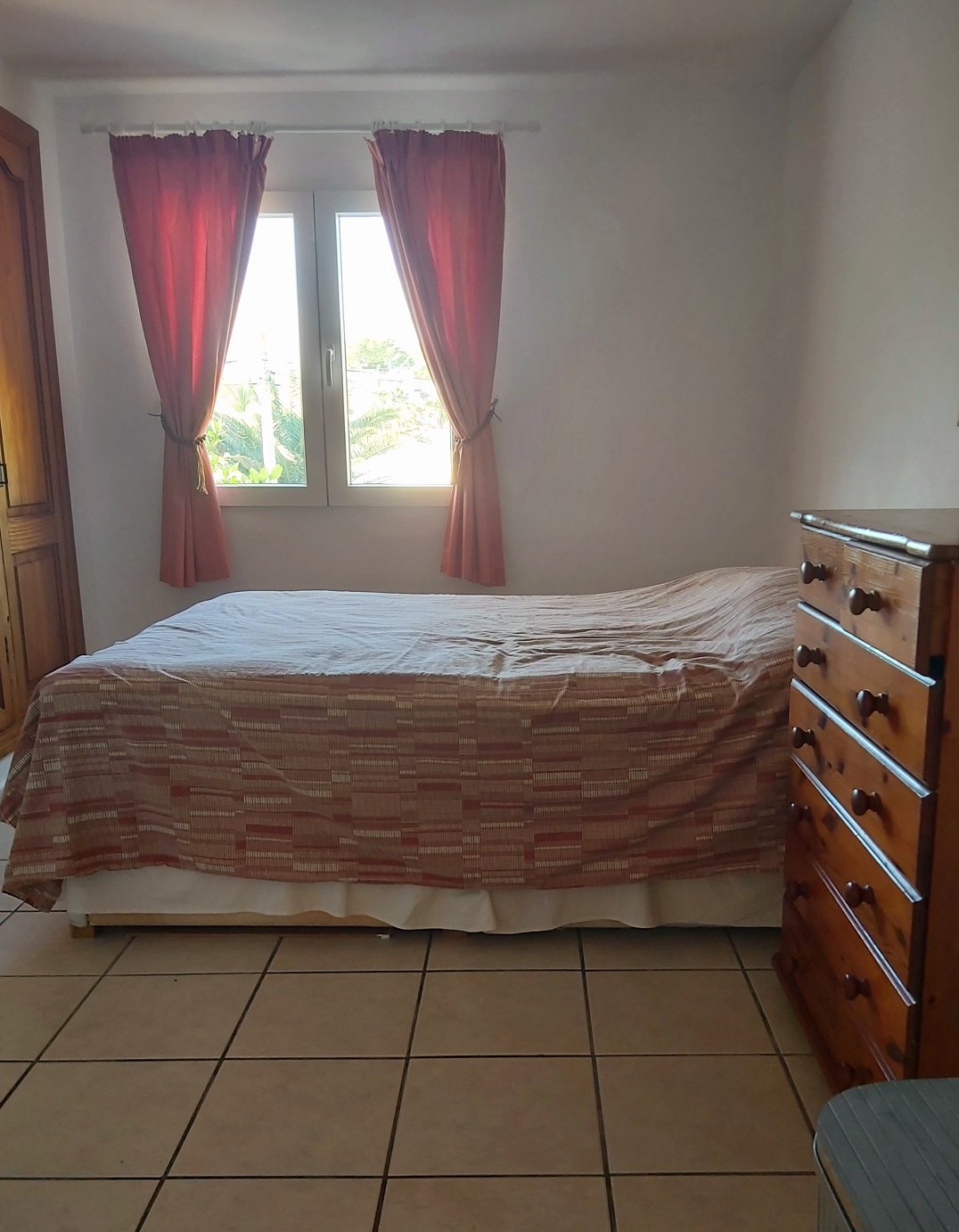 Bedroom with bed, wooden dresser, and window with red curtains